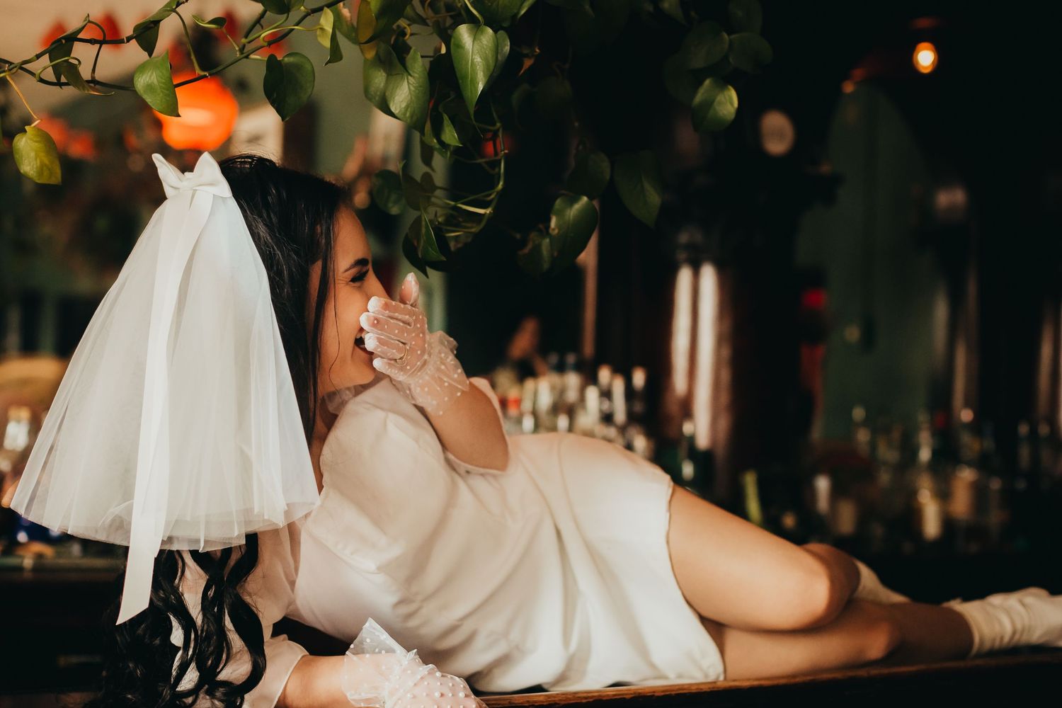 A bride in white dress reclines under citrus trees with twinkling lights.