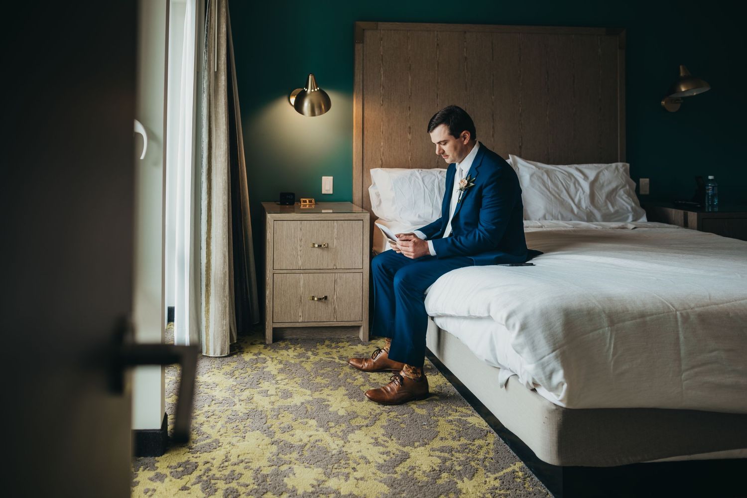 Hotel room interior with navy walls showing a bed and reading lamp.