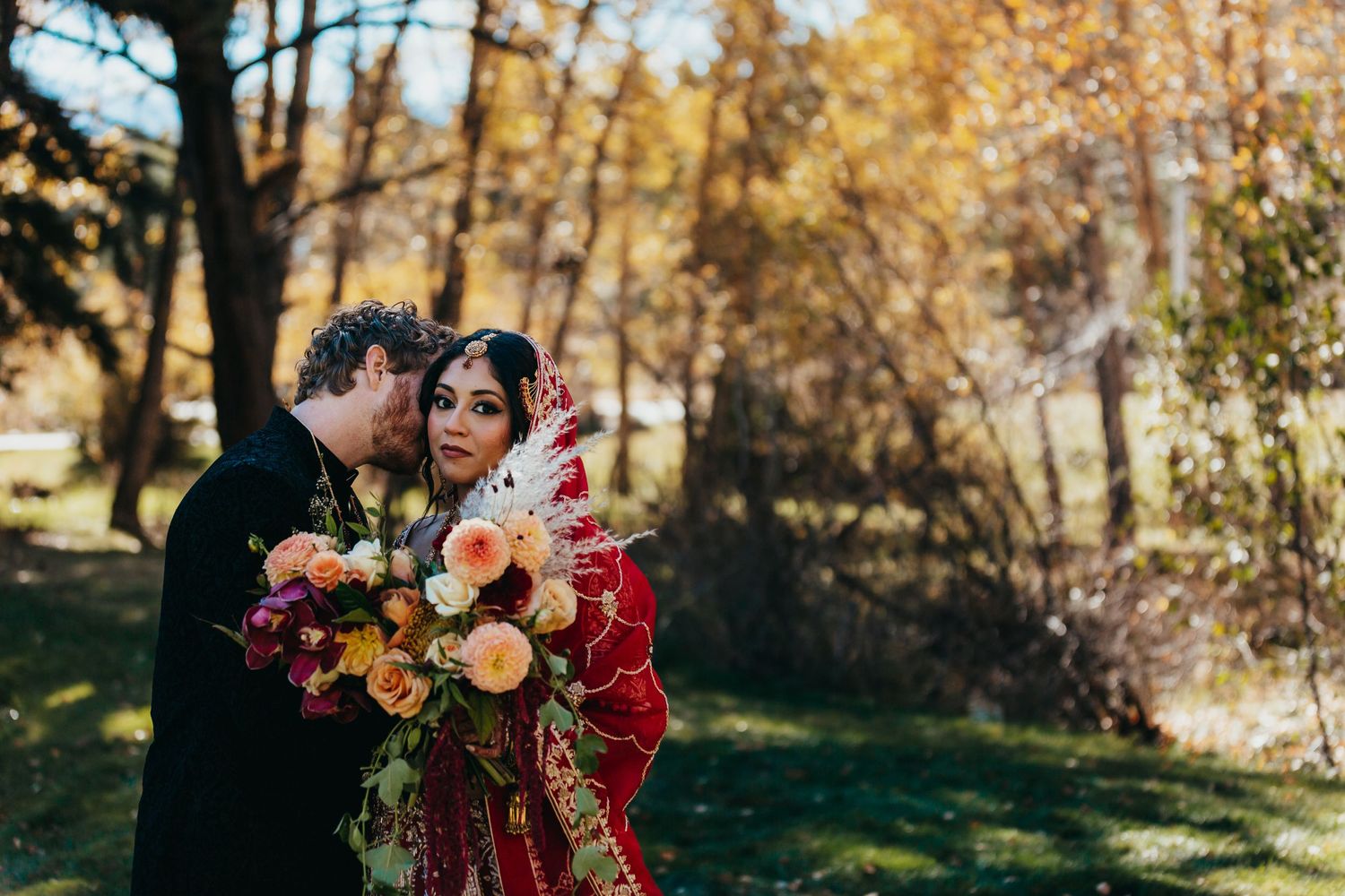 Wedding couple embraces while holding colorful bouquet in autumn forest.