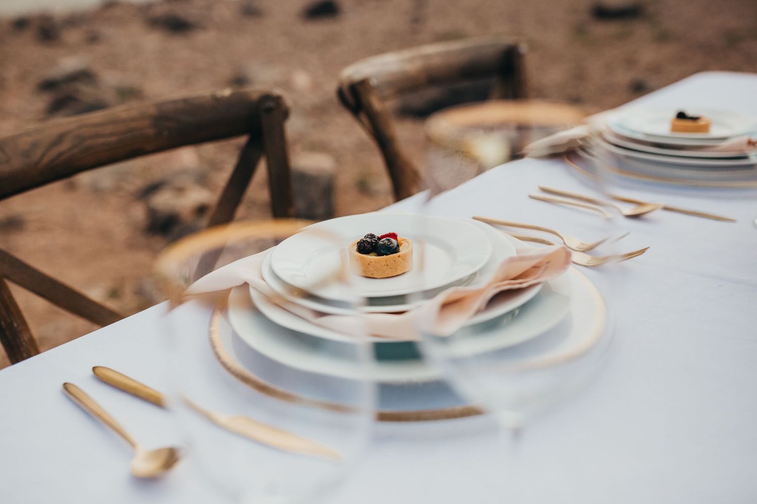 Minimalist place setting with stacked plates and blueberry garnish on white tablecloth.