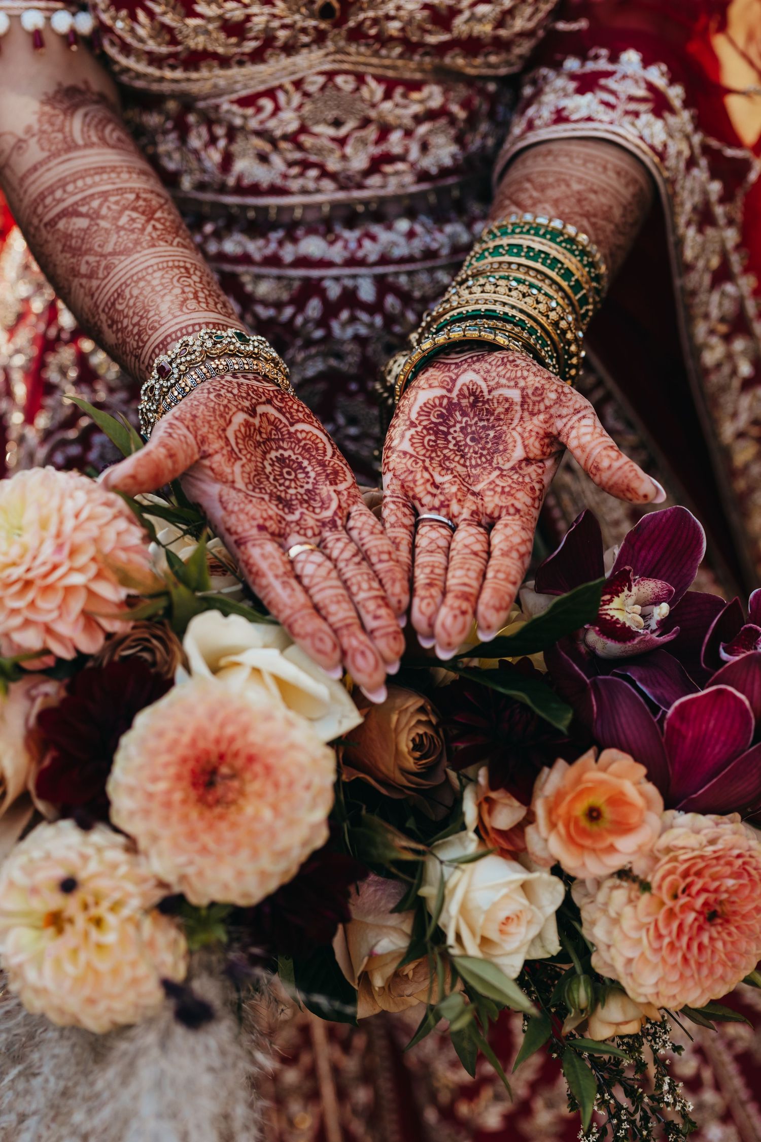 Detailed view of traditional henna designs on hands with bangles and wedding flowers.