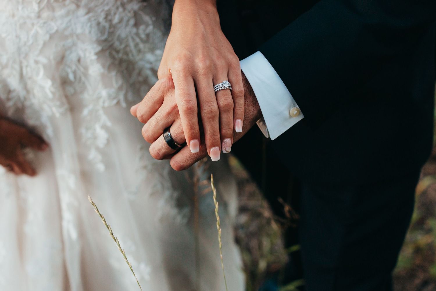 Close-up detail shot of wedding rings and hands against white fabric.