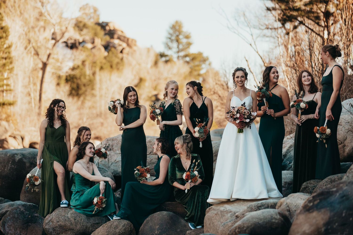Wedding party in dark dresses poses on rocky terrain during golden hour.