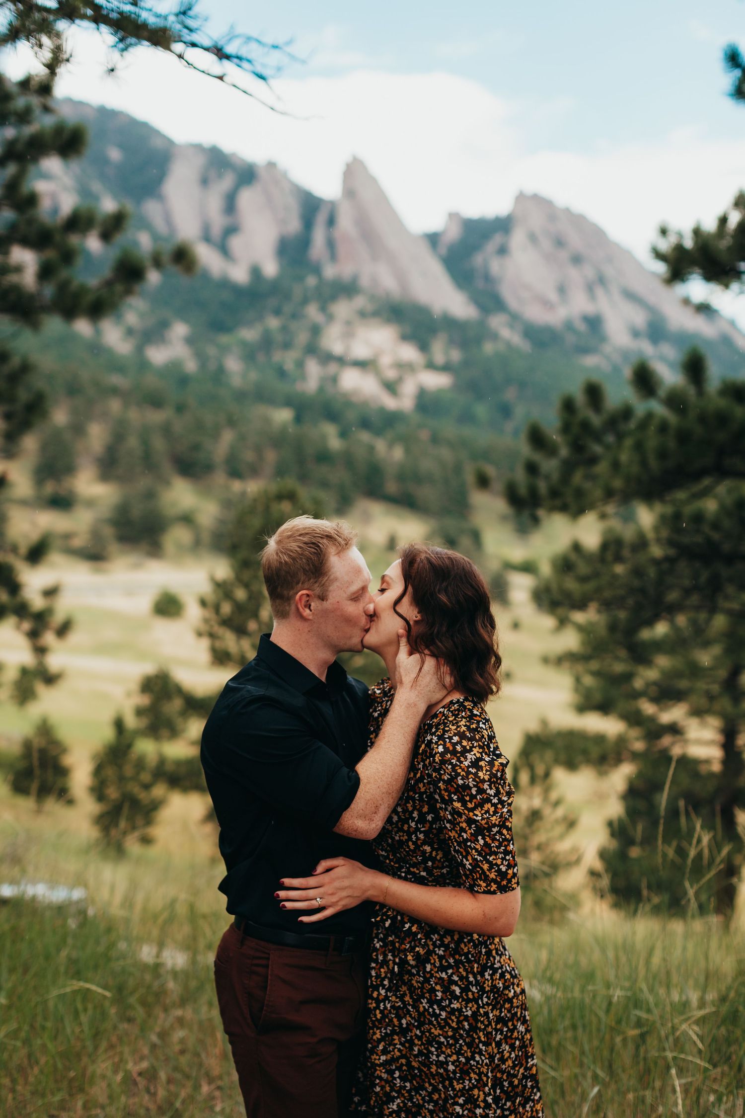 A romantic couple embracing and kissing with the Flatirons mountains of Boulder, Colorado in the background.