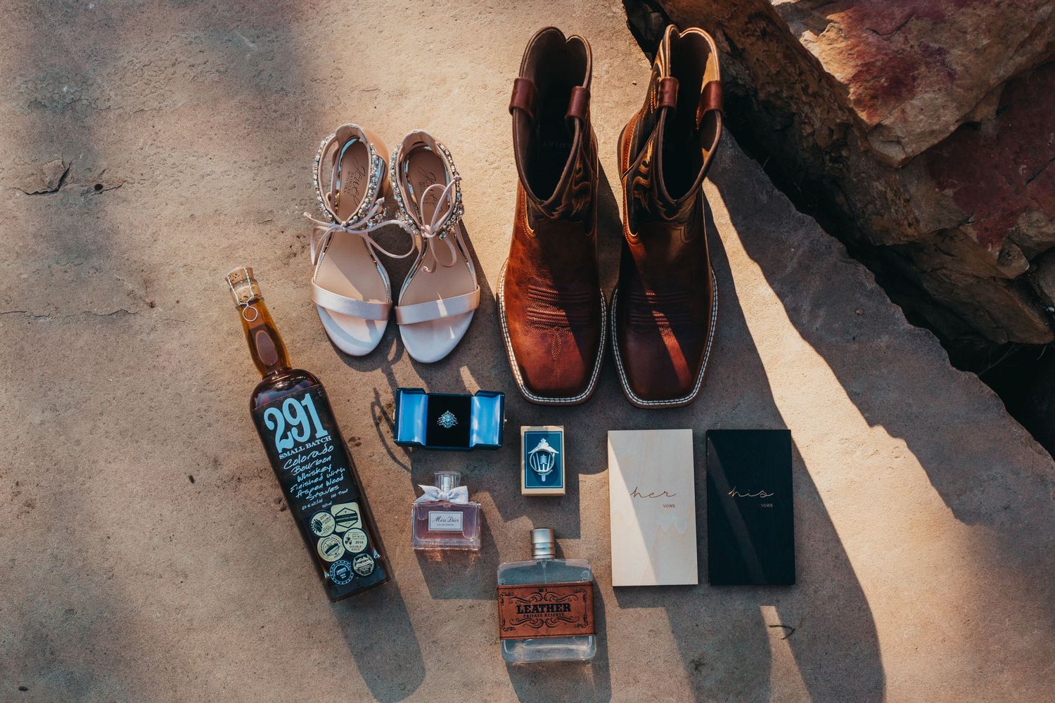 Wedding day accessories including shoes, perfume bottles, and rings arranged on concrete surface.