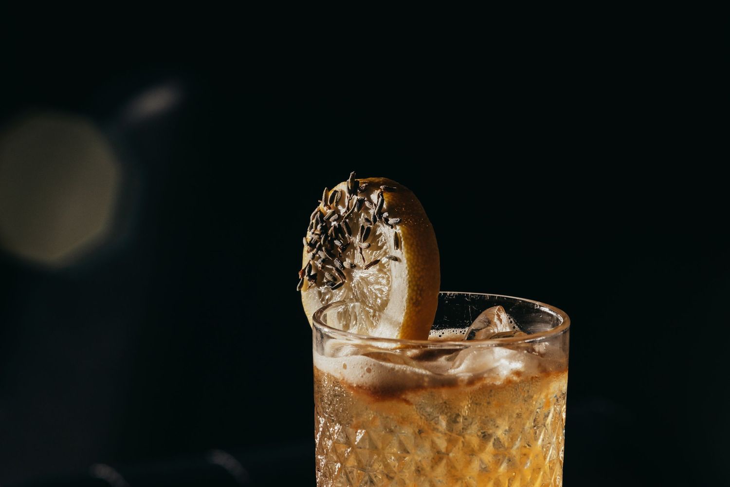 An elegant cocktail with ice and garnish in a cut crystal glass against a dark background.