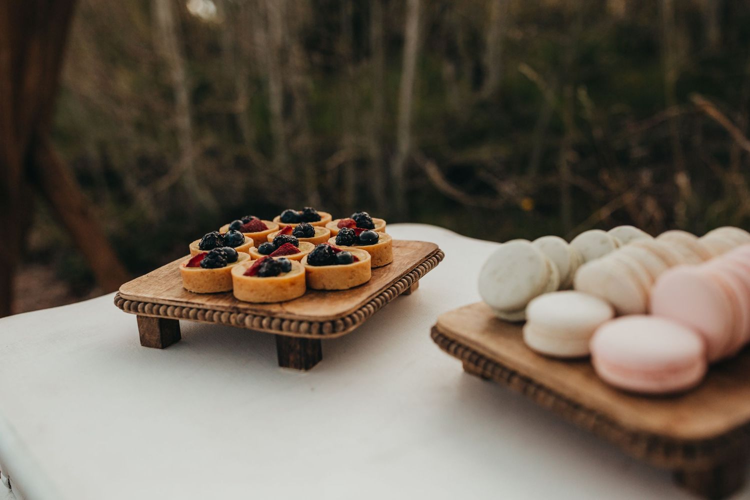 Dessert display featuring macarons and dark berries on wooden serving boards.