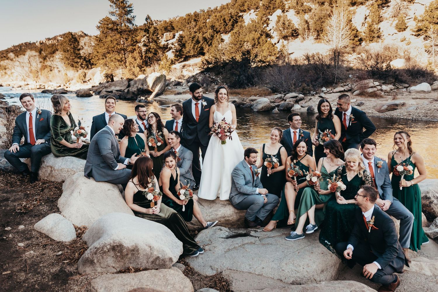 Wedding party in navy and emerald attire posed on rocky terrain at sunset.