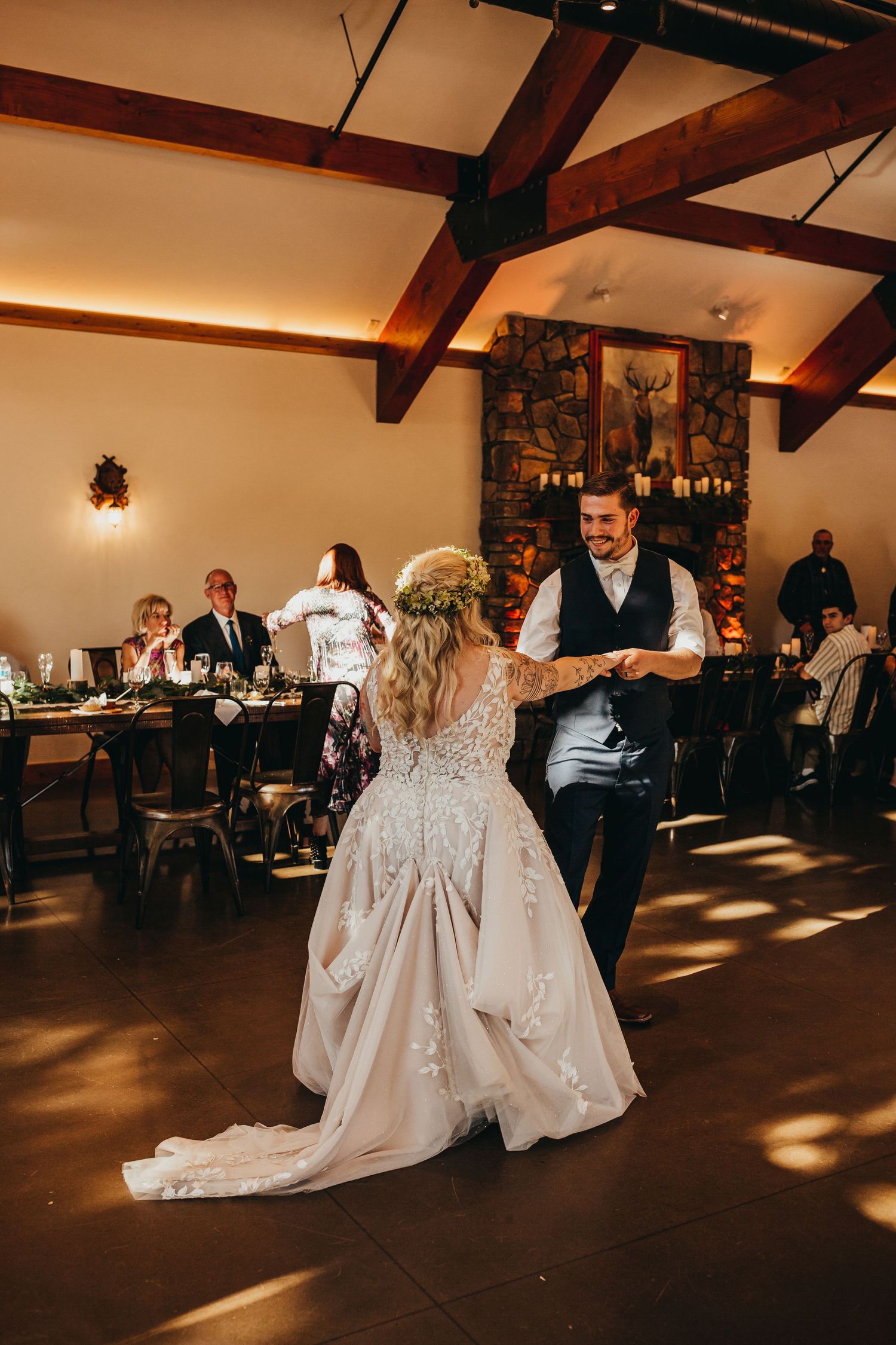 Couple dancing at wedding reception in rustic venue with exposed wooden beams and romantic lighting.