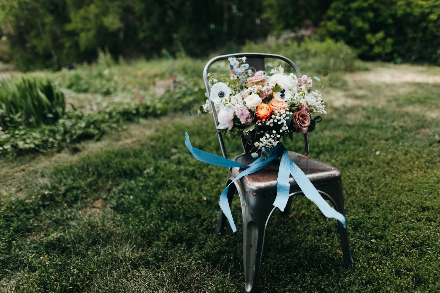 Wedding bouquet with blue ribbons arranged on metal chair outdoors.