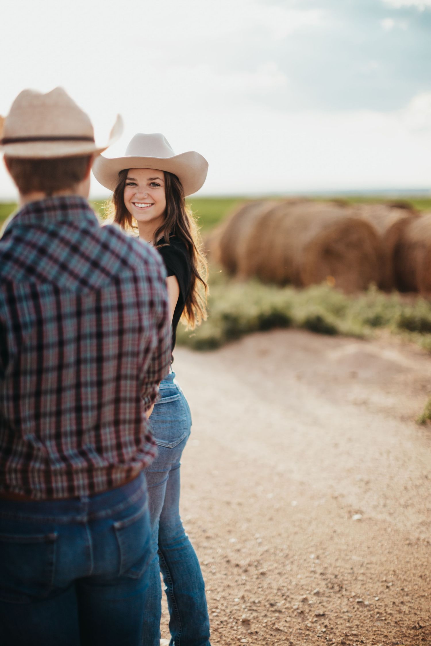 Western-styled couple conversing on a dirt path with hay bales in the background.