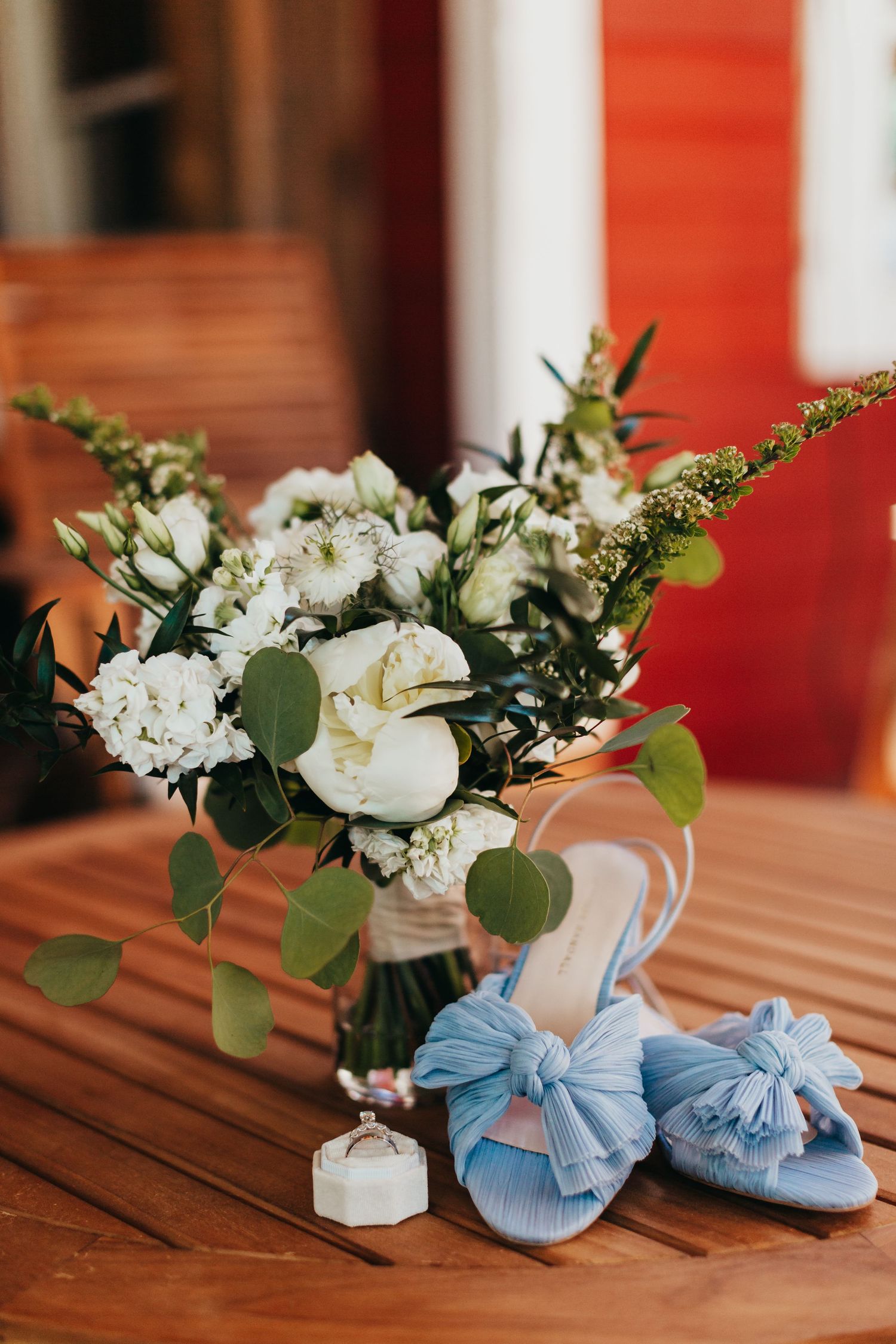White floral bouquet arrangement with blue bow shoes on wooden table.