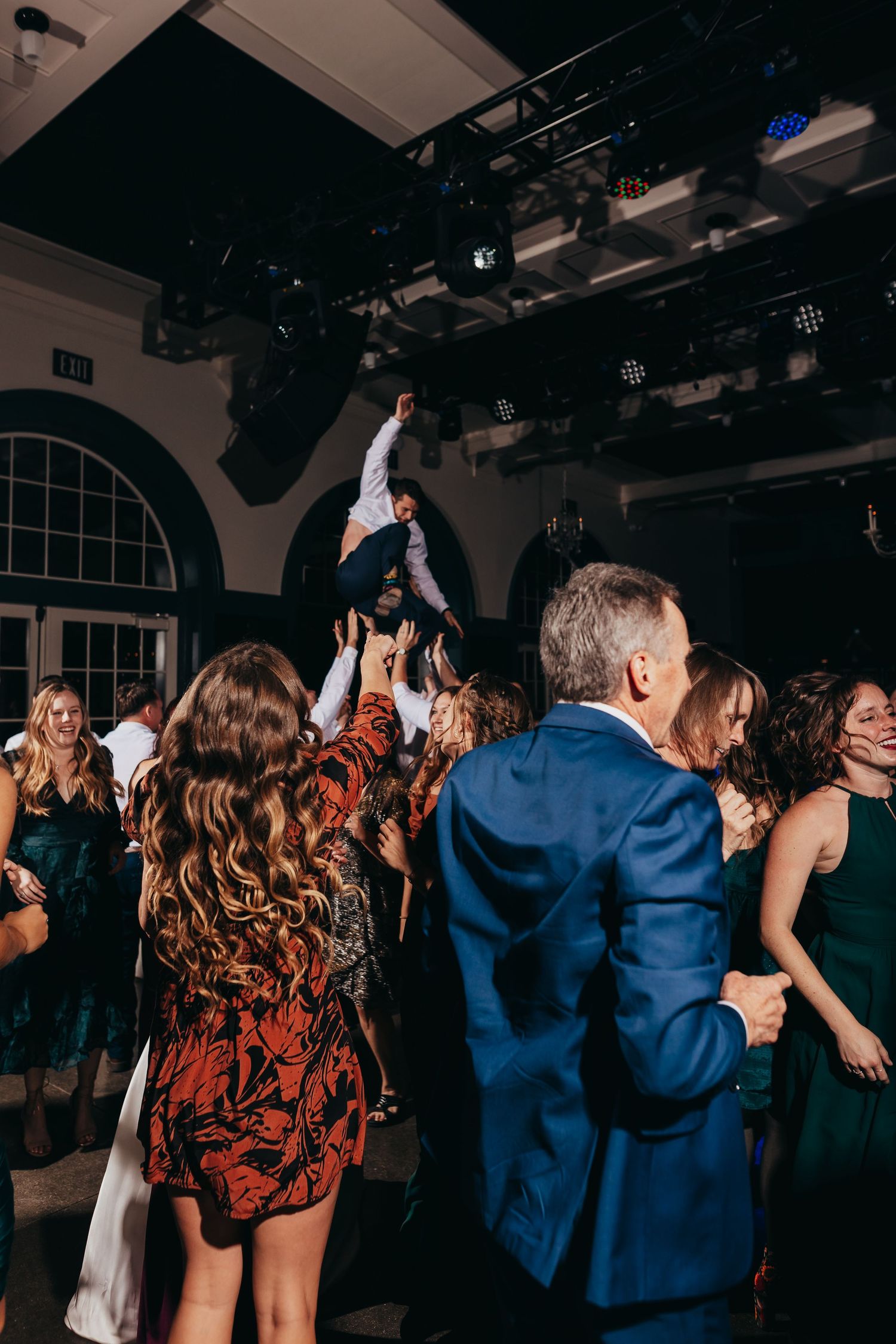 Wedding guests dancing energetically at reception with person lifted overhead.