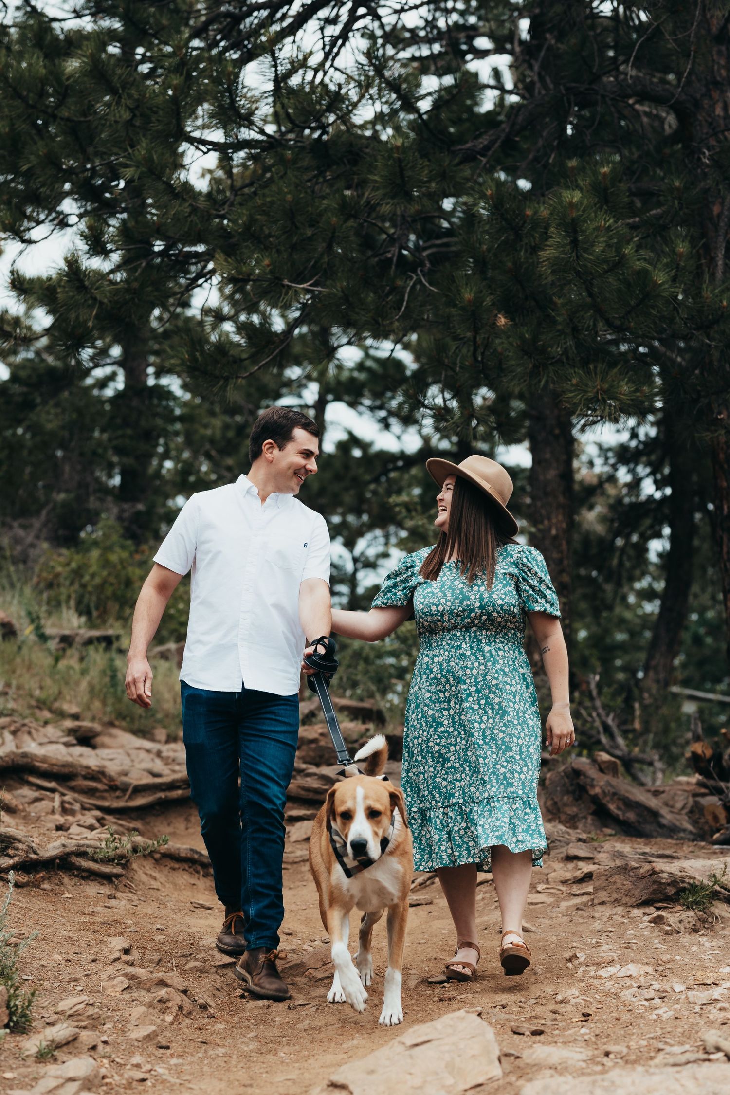 Couple walks dog on hiking trail through pine forest.