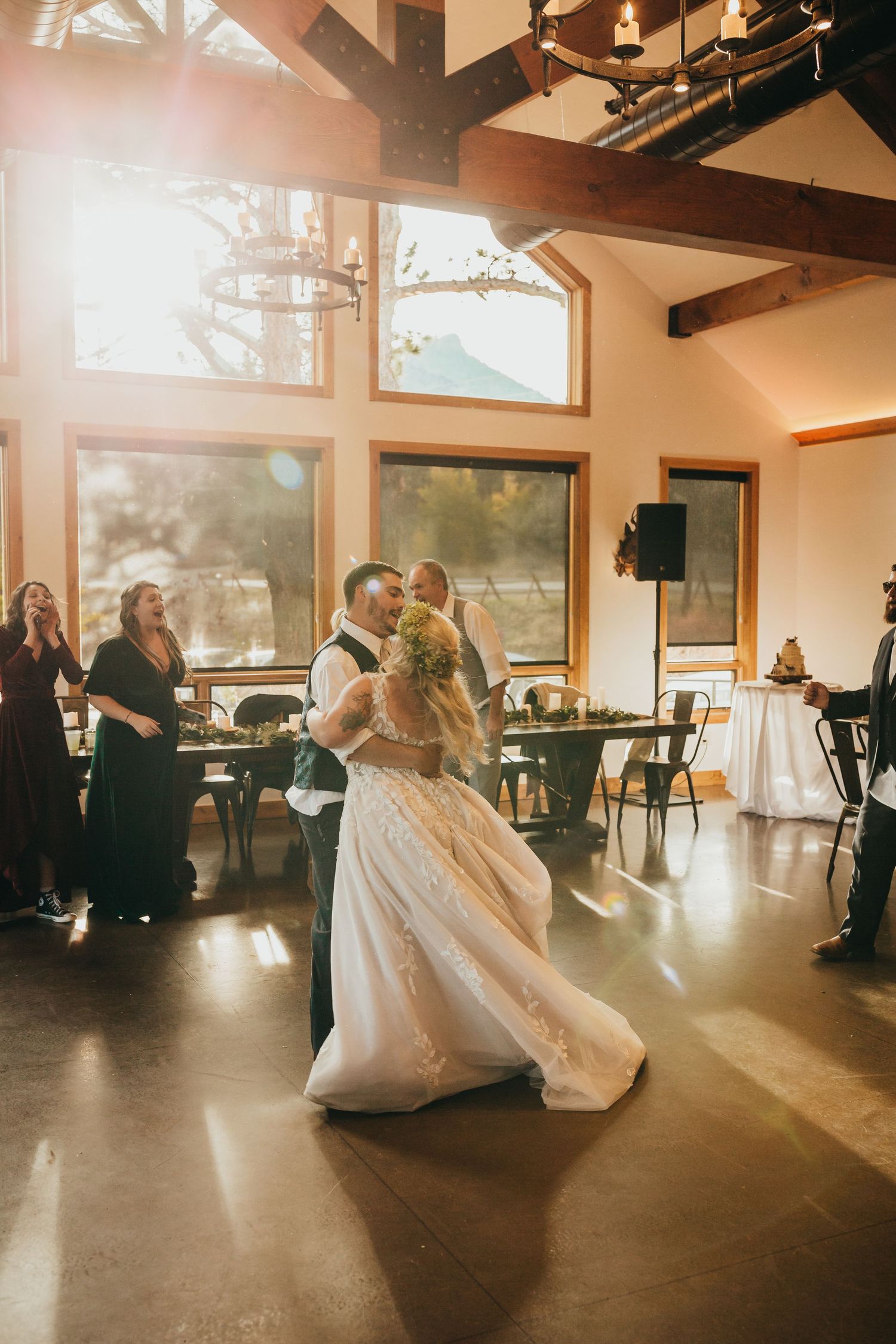 A couple shares their first dance in a sunlit venue with high ceilings and exposed beams.