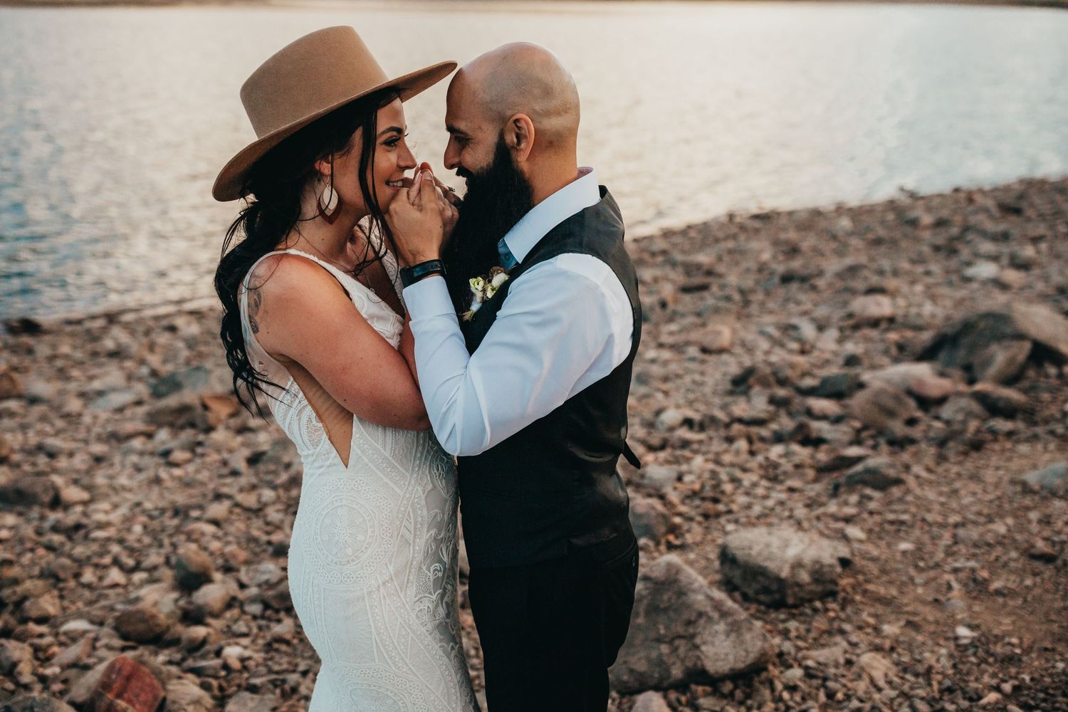 Romantic wedding portrait with brown hat and lace dress against lakeside setting.