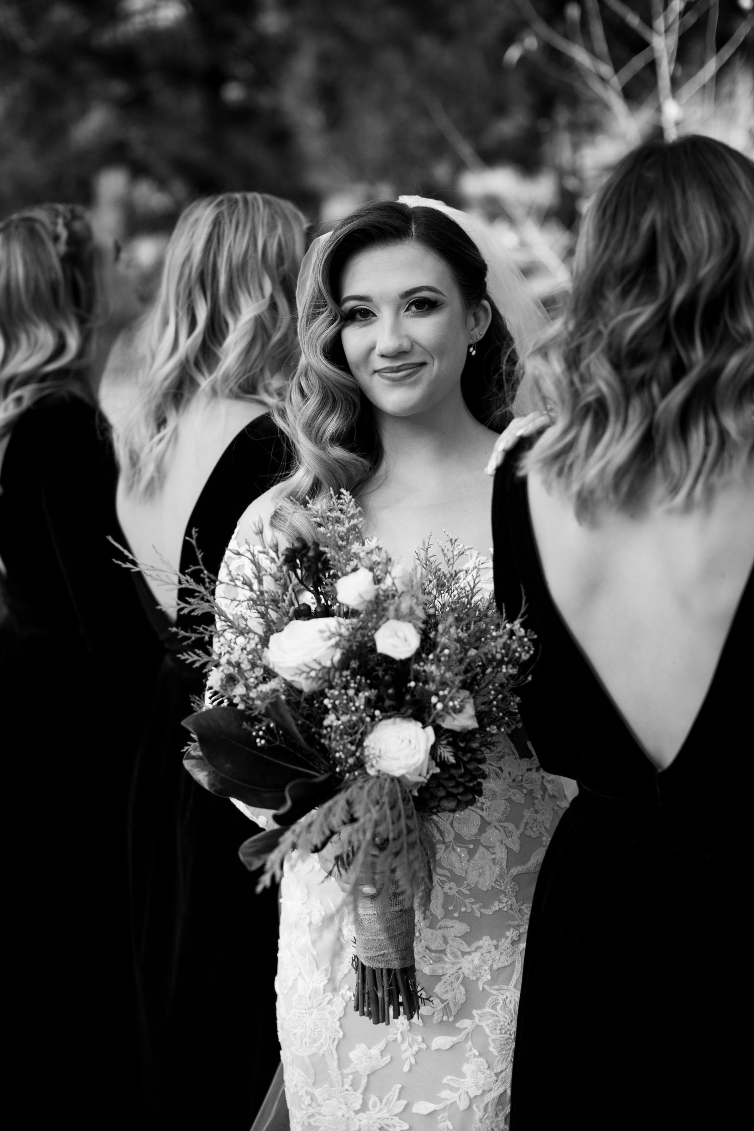 Elegant wedding party portrait with bride in white lace dress surrounded by bridesmaids in black dresses.