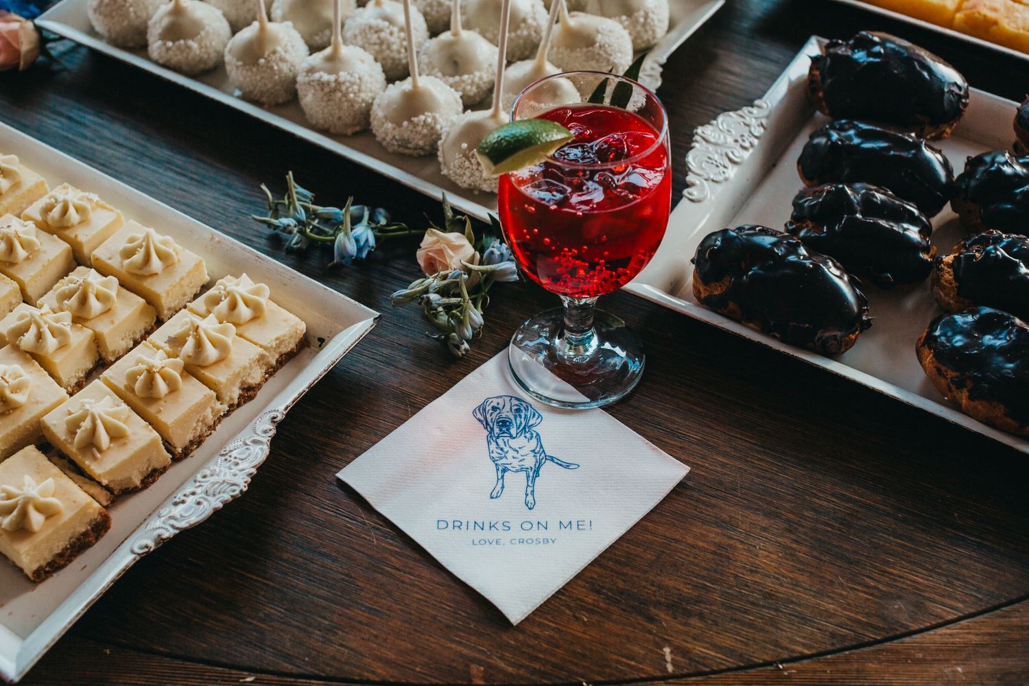 Wedding reception dessert table featuring a red cocktail and custom napkin with illustration.