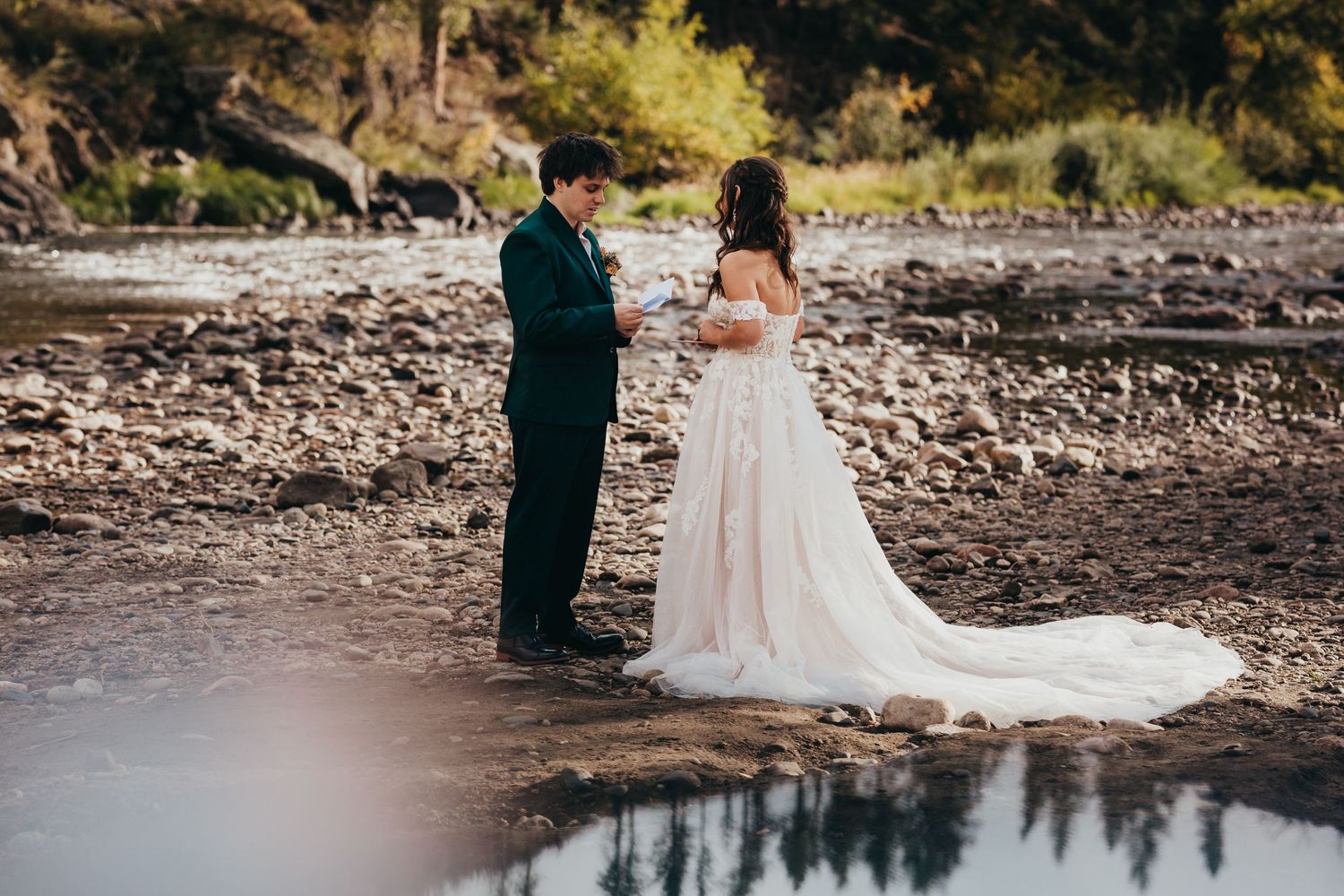Bride and groom share a private moment by a reflective pond.