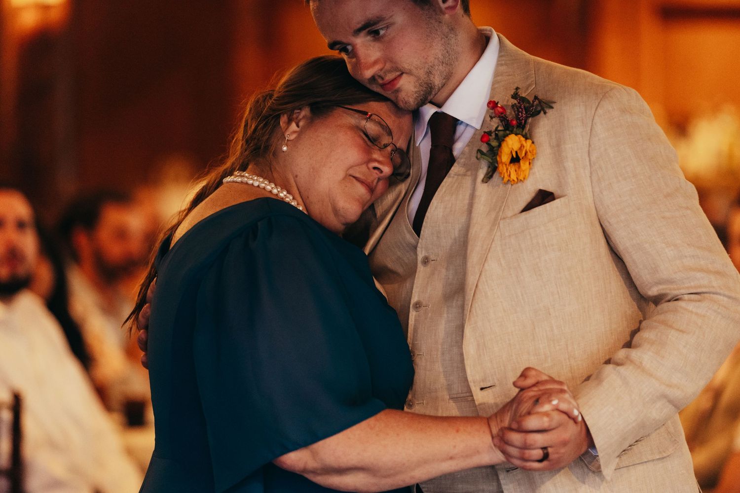 A tender dance moment between a couple at a wedding reception with warm lighting in the background.