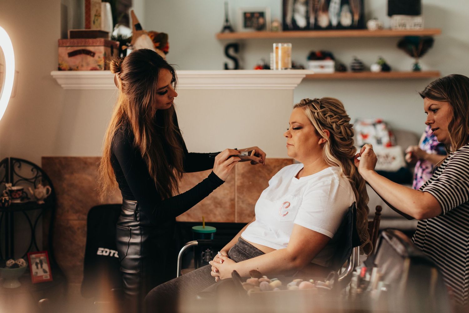 Hair and makeup artists working on styling preparation in a bright room.