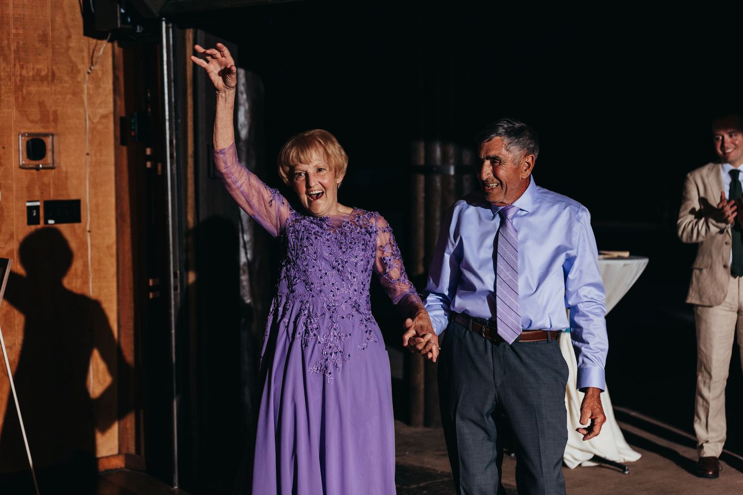A couple shares a joyful dance moment in purple attire at an indoor reception.