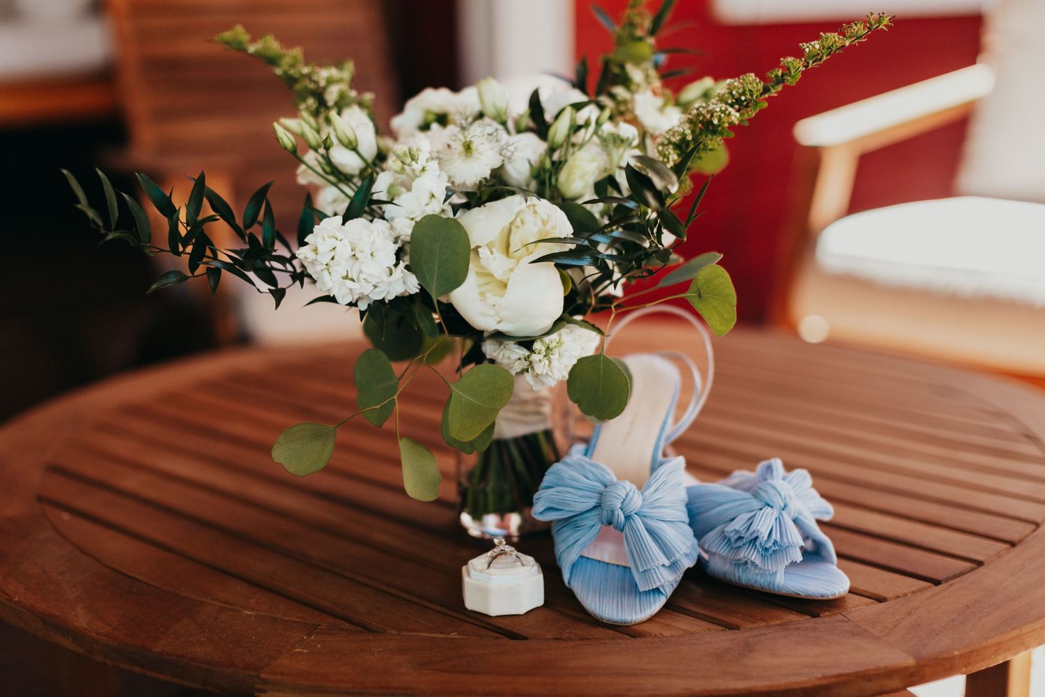 White floral arrangement with baby blue shoes and delicate wedding accessories on wooden table.