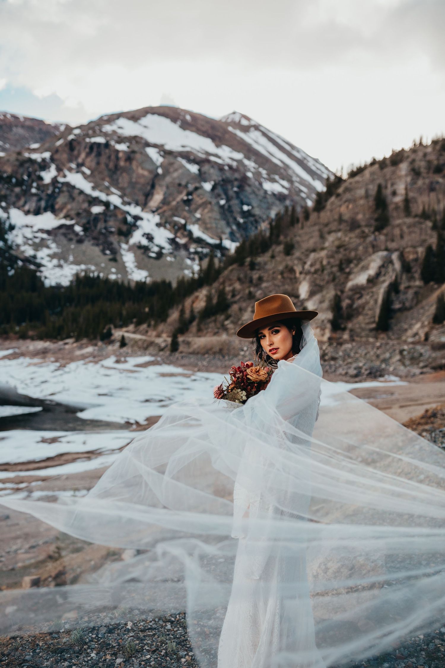 Dramatic mountain wedding photo with flowing veil and dried flower bouquet.