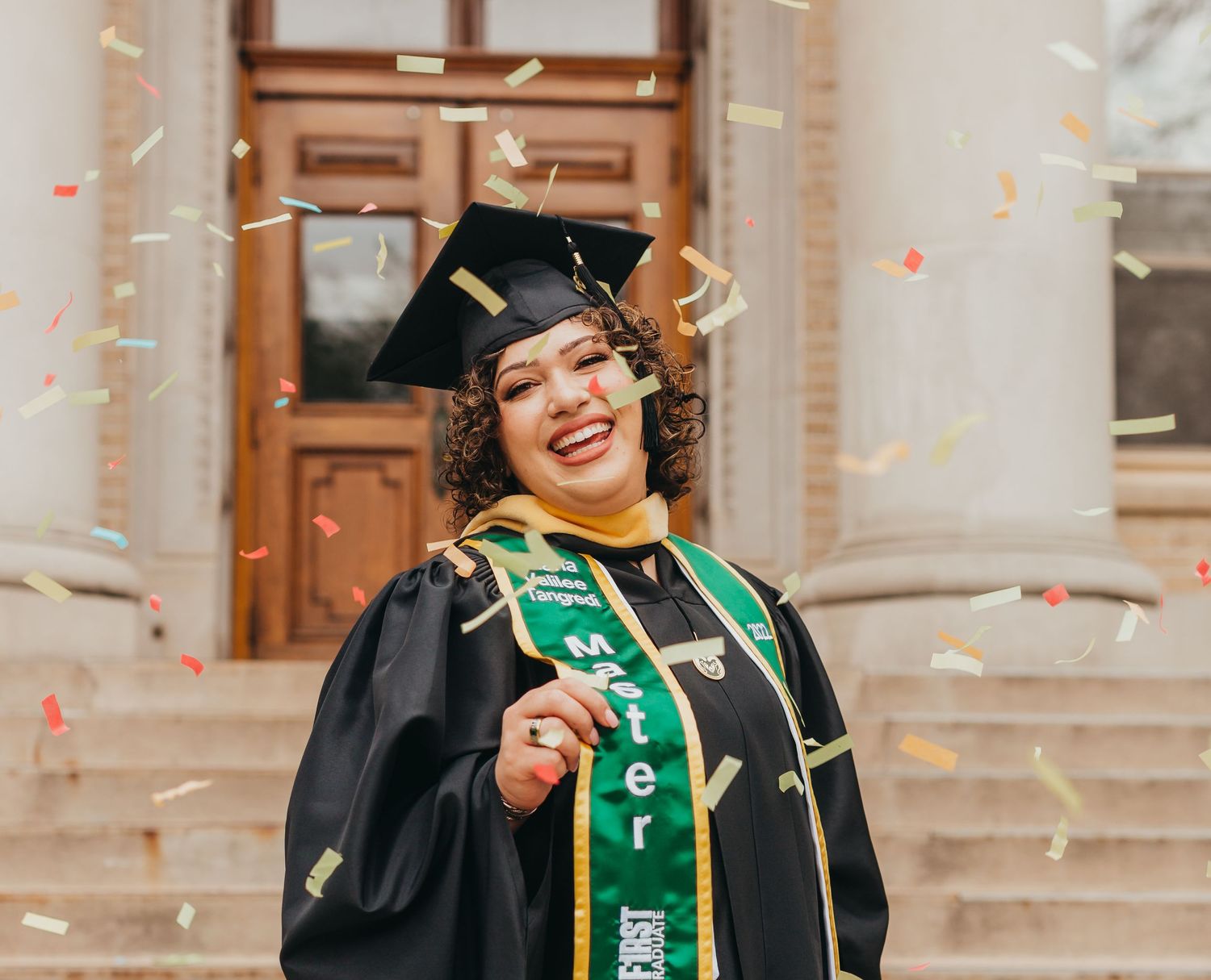 Graduate in cap and gown celebrating with confetti at commencement ceremony.