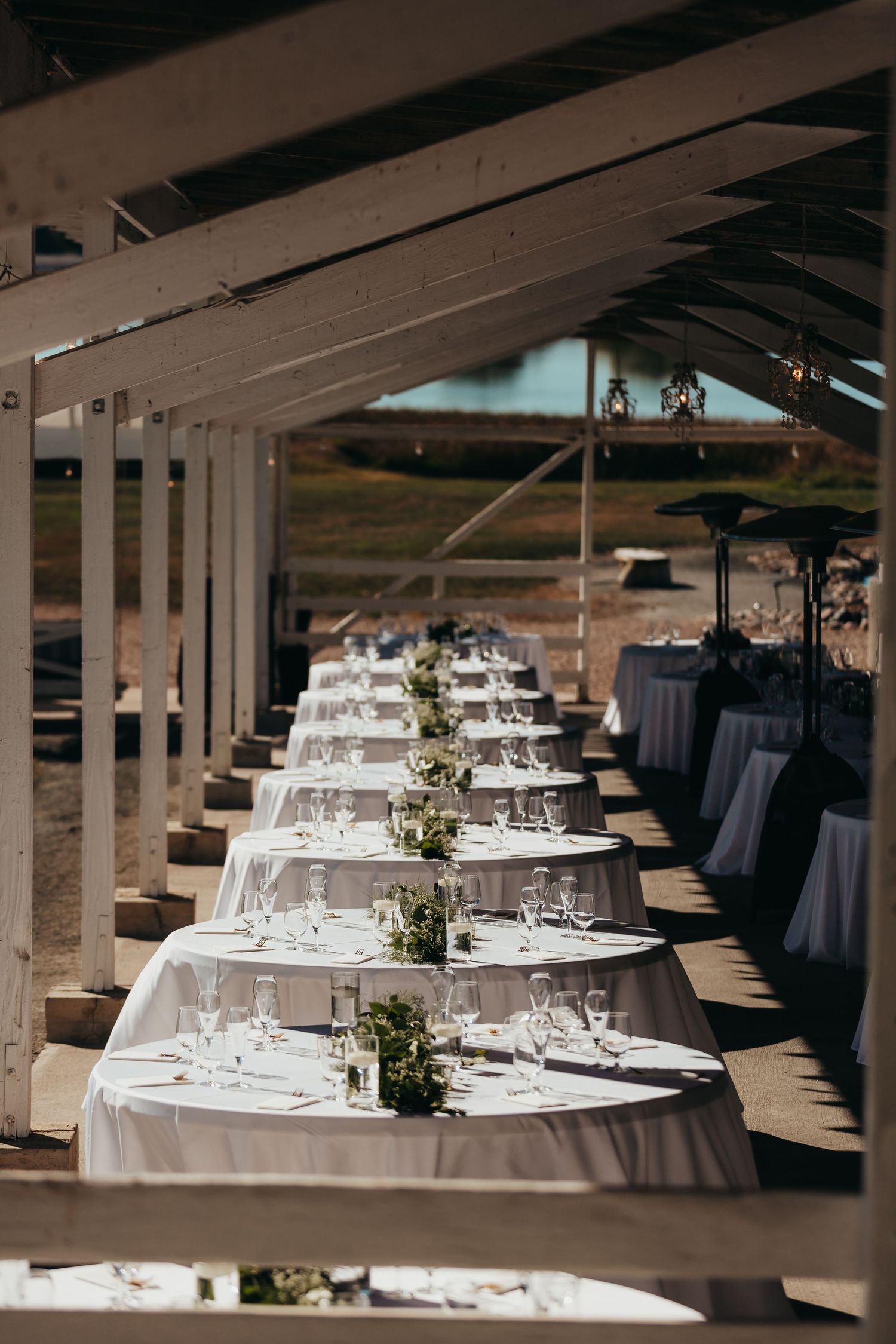 Elegant wedding reception table settings with white linens and small centerpieces under a covered venue.
