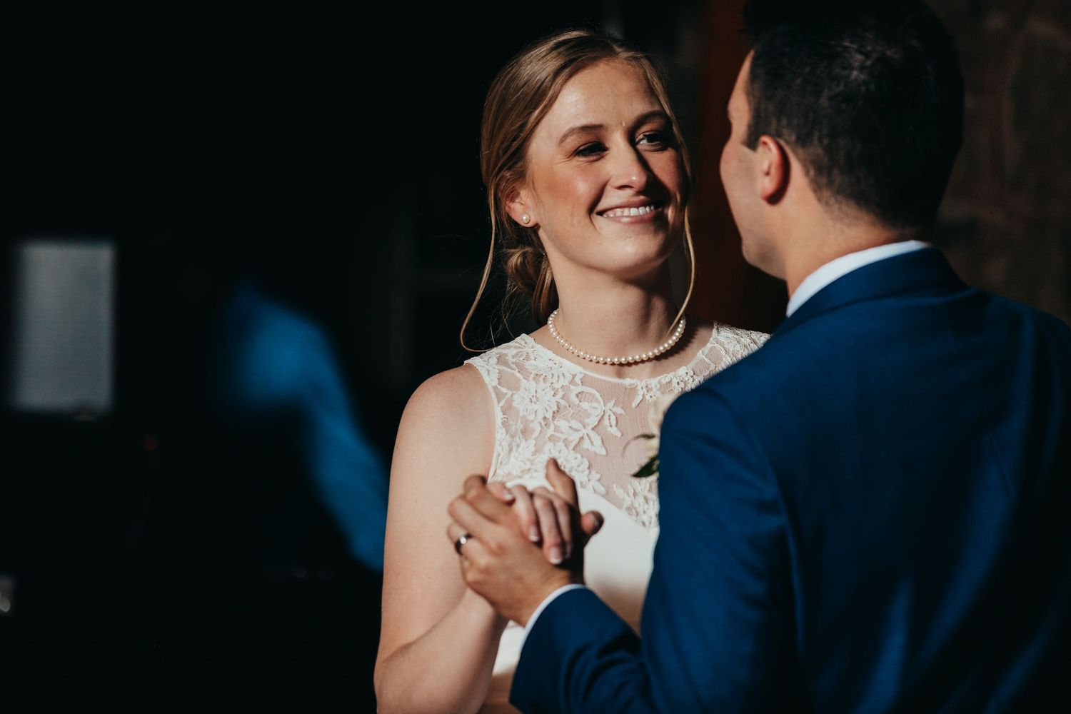 A tender moment between newlyweds dancing together, with the bride wearing a white lace dress.