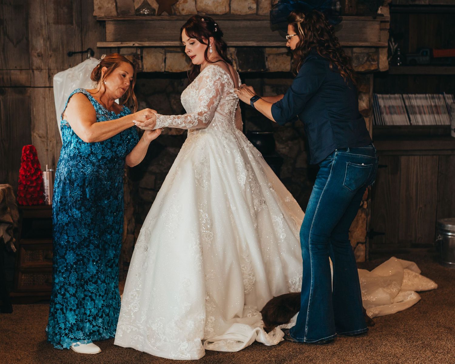 Wedding dress fitting session with helpers making final adjustments in rustic venue.