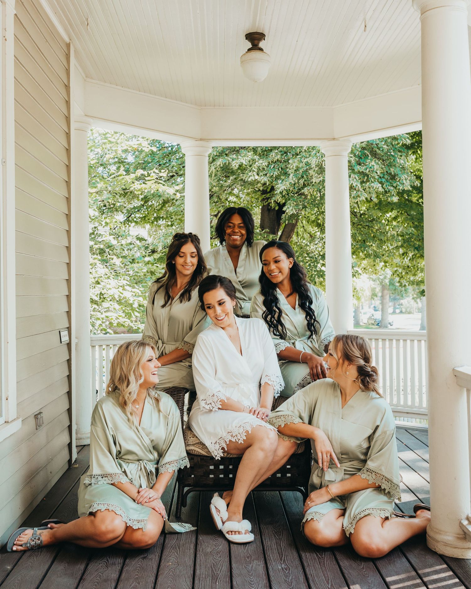 Wedding party in matching robes gather on a bright white porch for pre-ceremony photos.