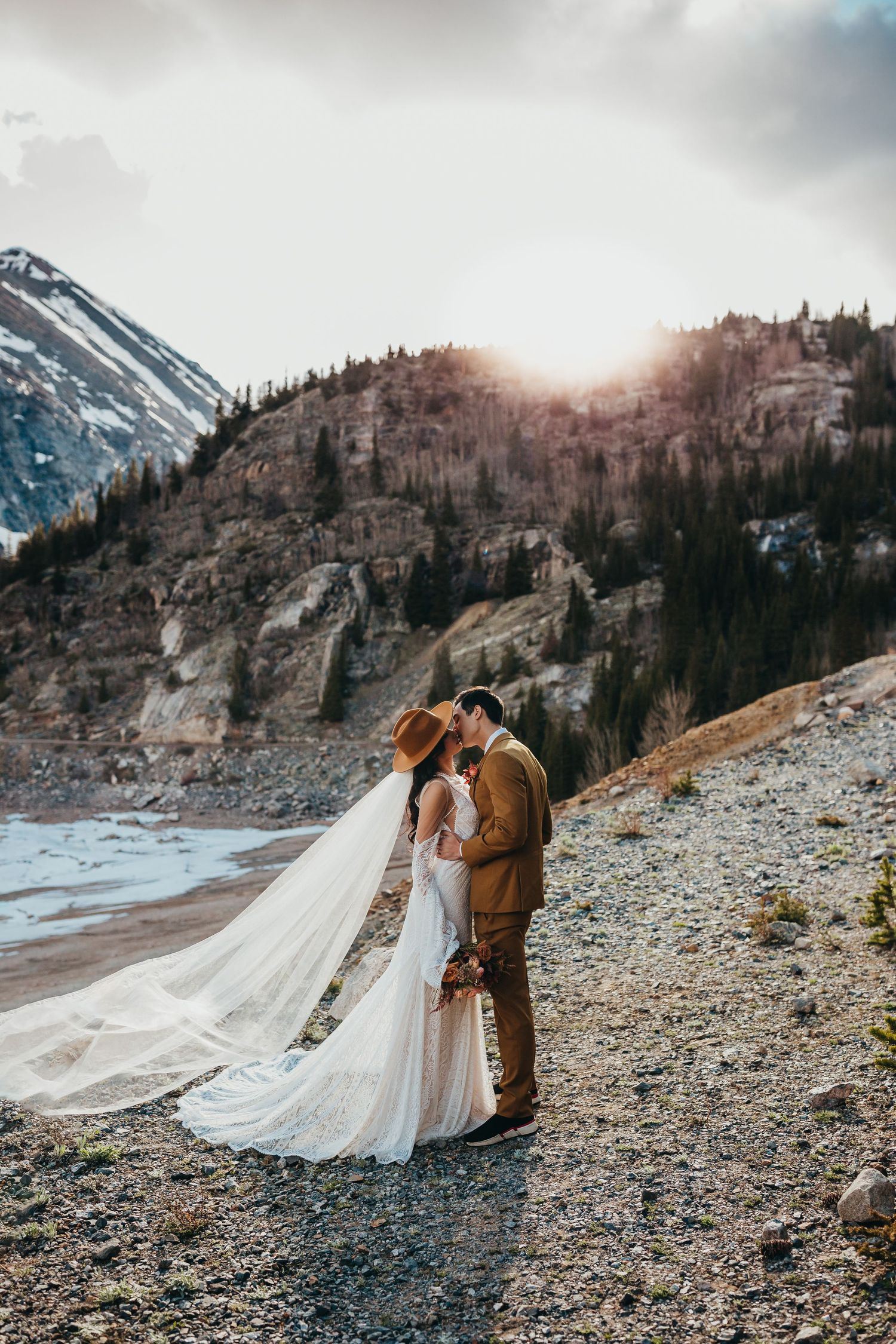 A sunset wedding portrait with dramatic mountain backdrop and flowing veil.