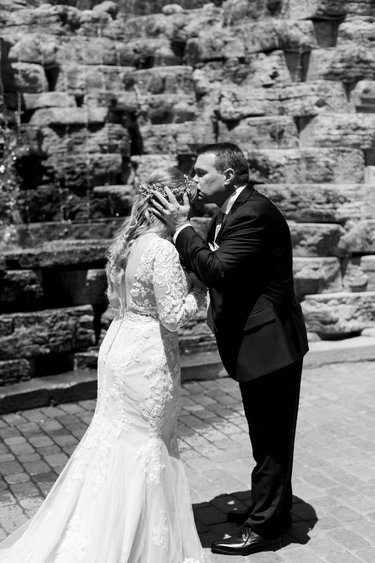Black and white portrait of couple sharing intimate moment against stone wall backdrop.