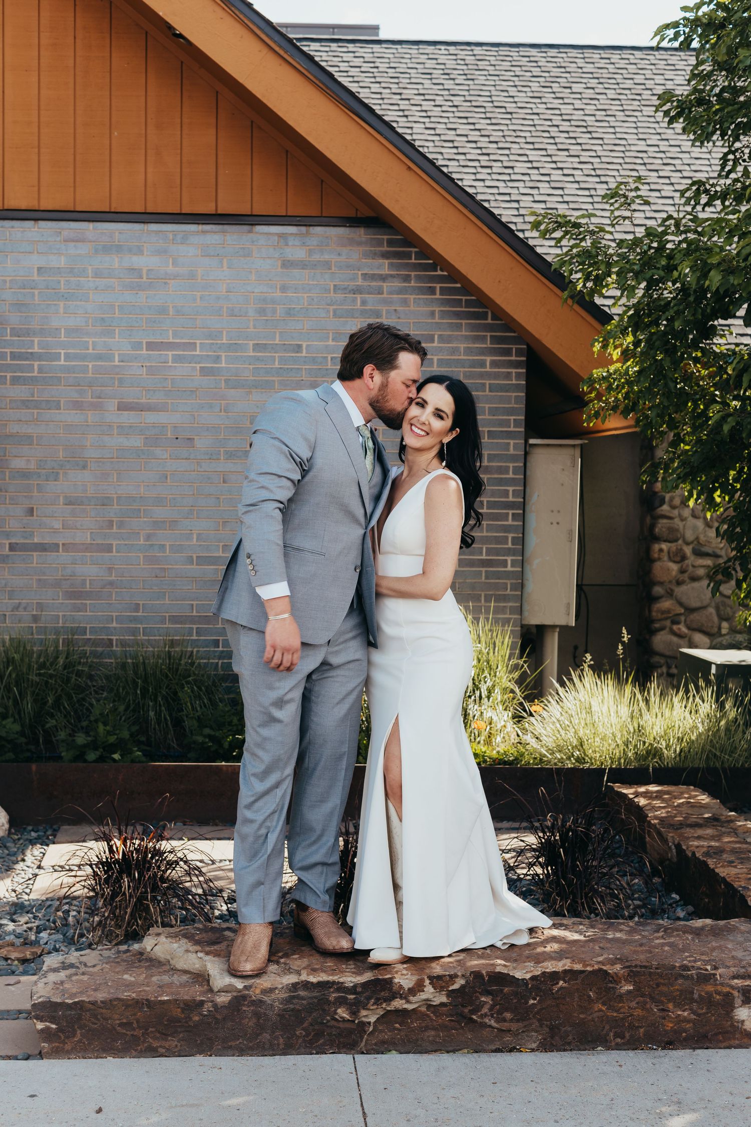Wedding couple in elegant attire posing against brick building exterior.