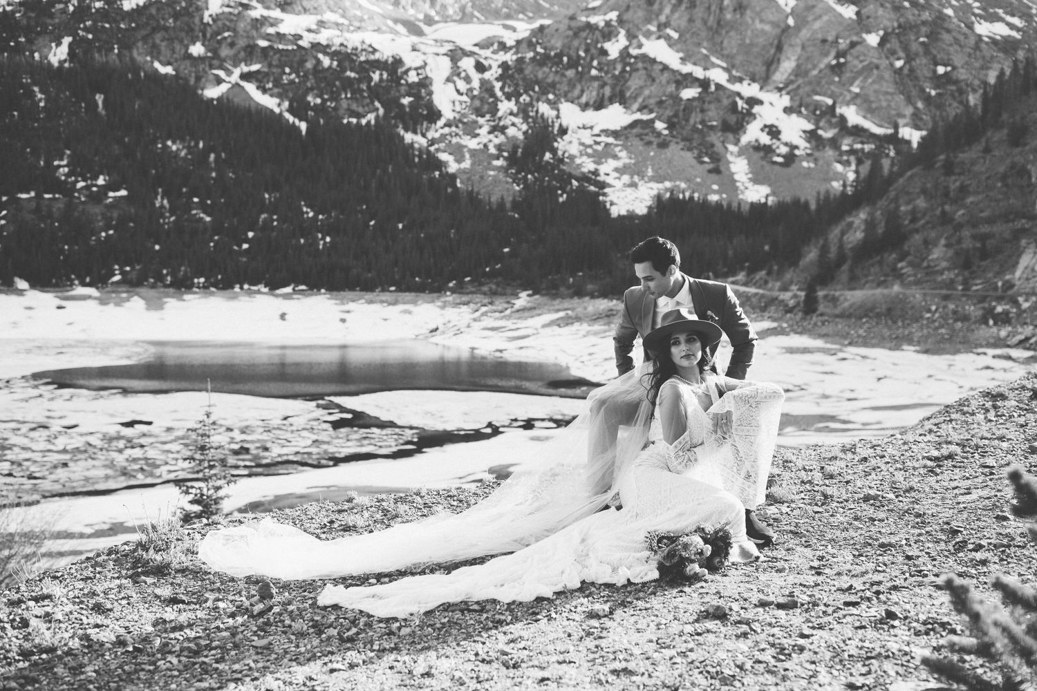 A black and white wedding portrait by a frozen mountain lake with flowing dress.