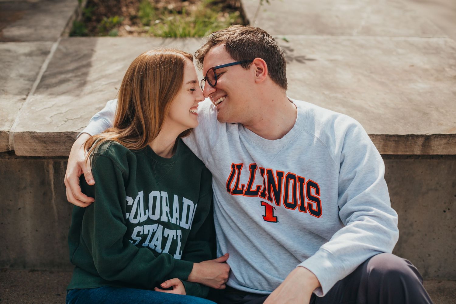 Two college students in university sweatshirts share a romantic moment on campus.