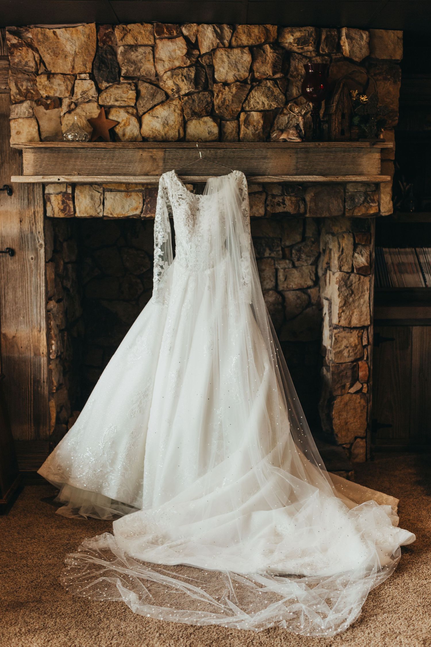 Elegant white lace wedding dress with long sleeves displayed against rustic stone fireplace.