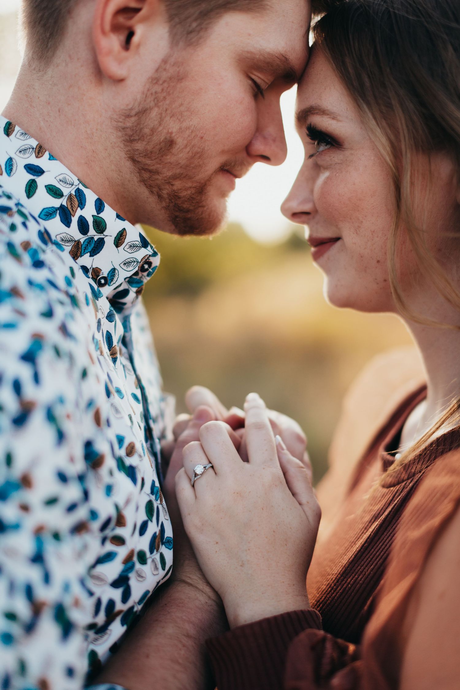 Intimate close-up of couple holding hands with engagement ring visible.