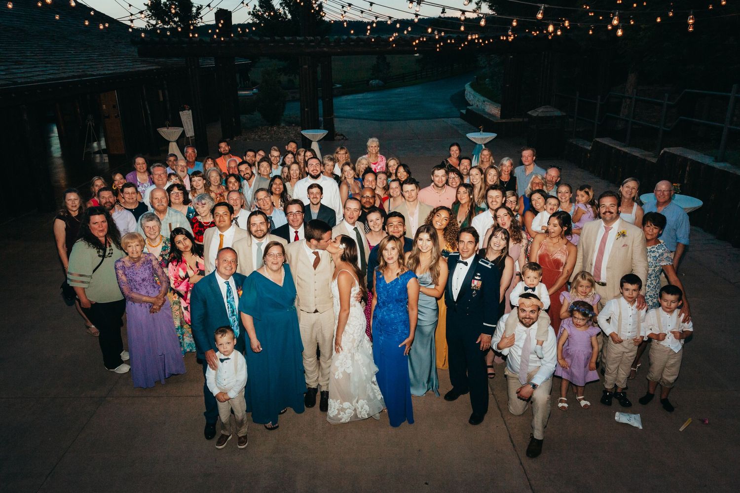 Large group photo of wedding guests gathered outdoors at dusk for a celebratory portrait.