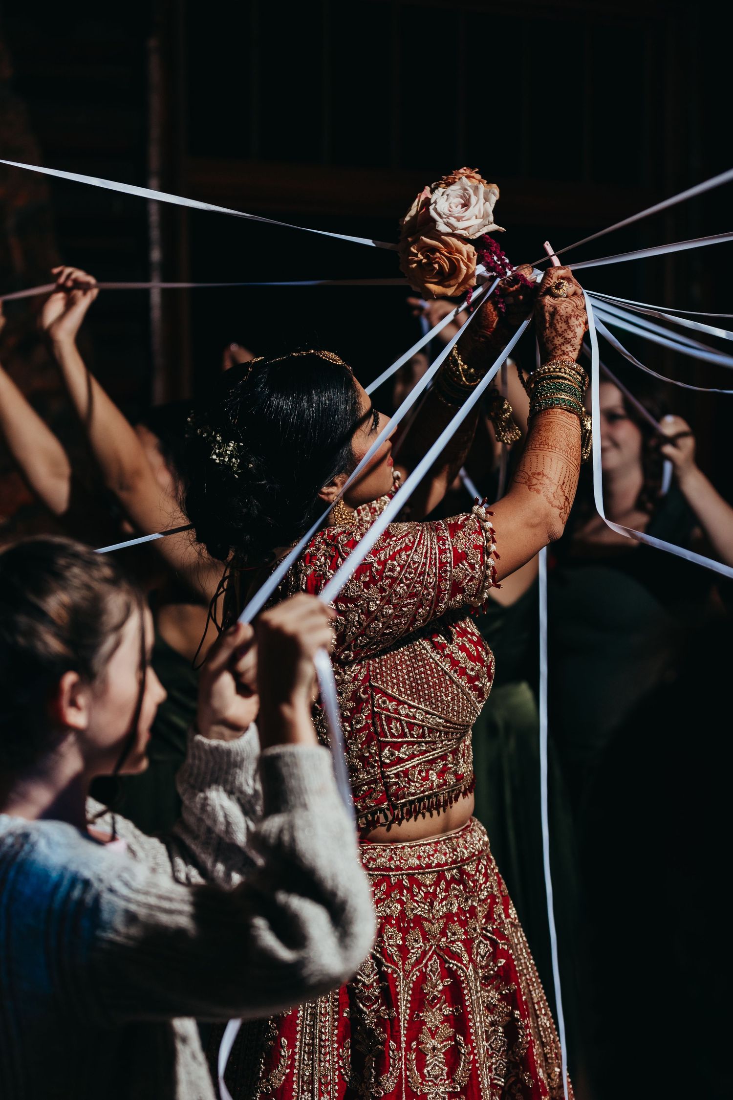Wedding guests participate in a traditional ribbon pulling ceremony with the bride in red attire.