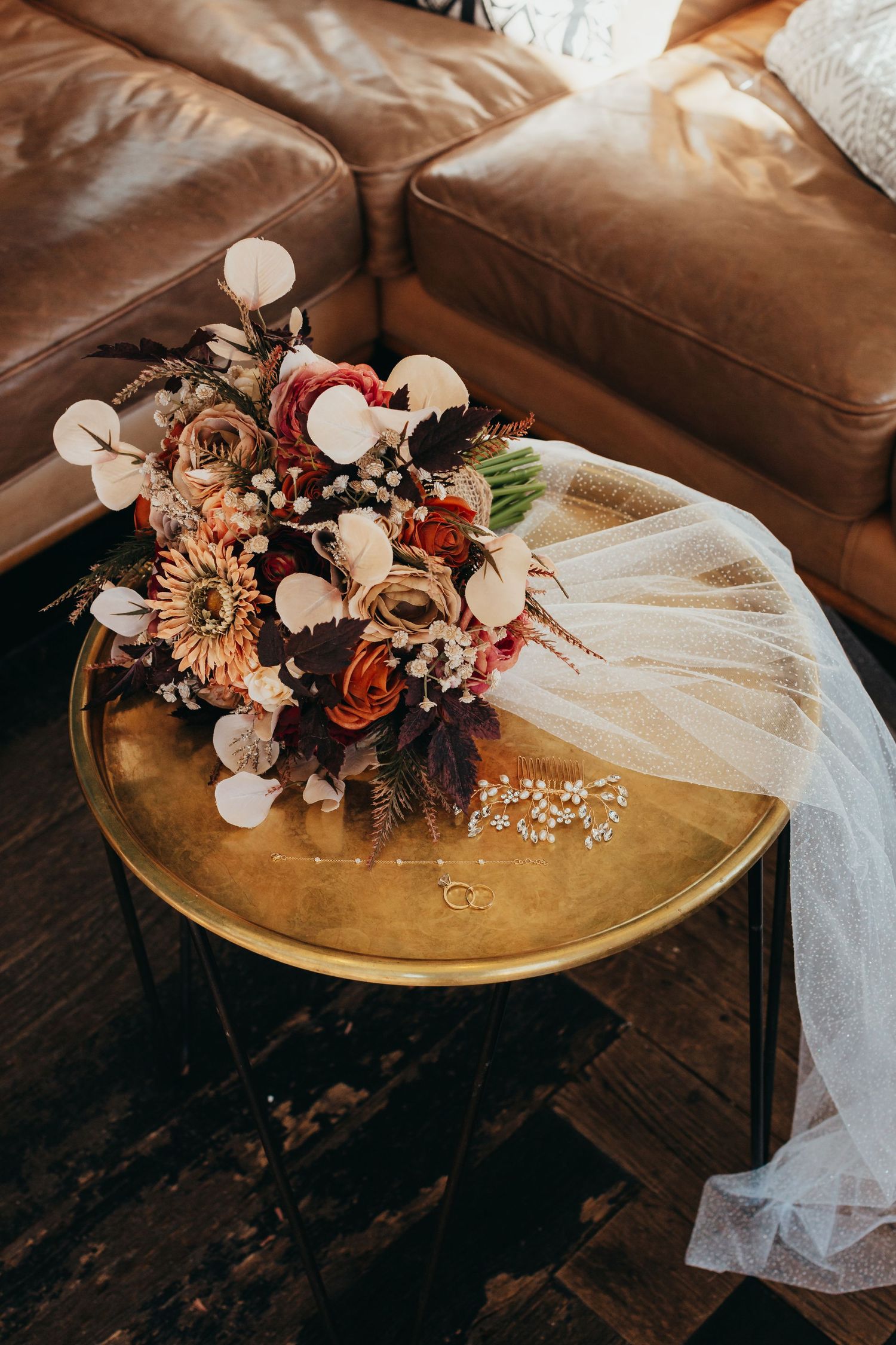 Wedding bouquet with dried flowers and veil on gold coffee table with leather couch.