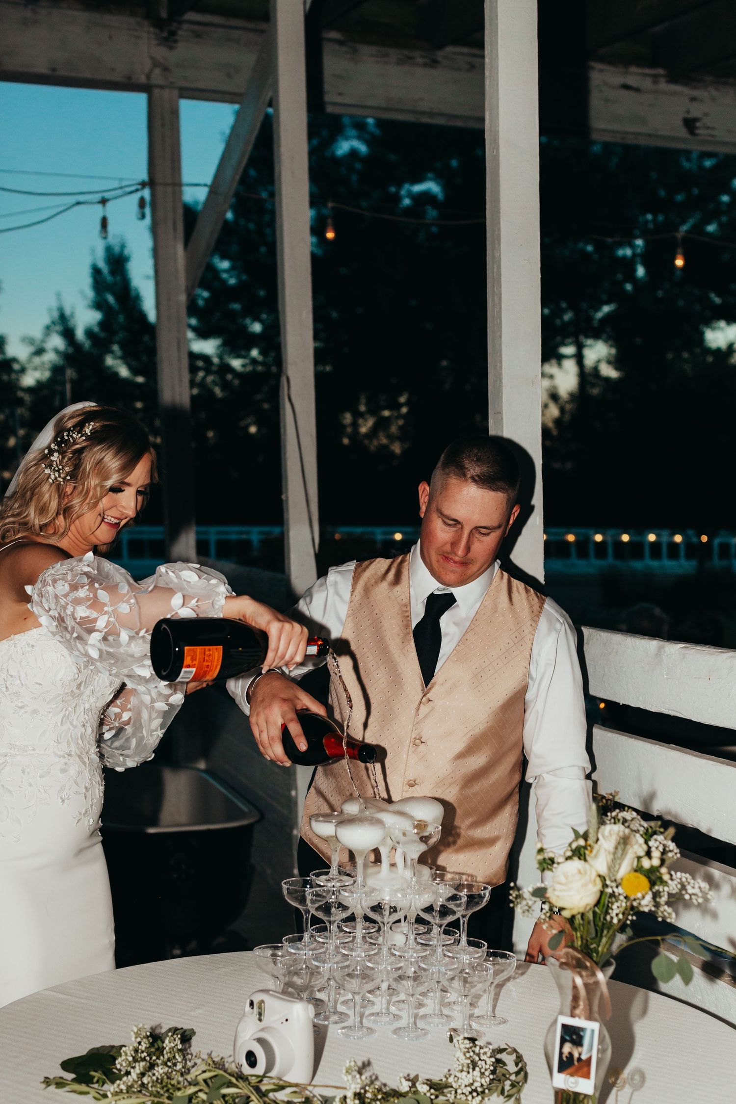 Couple pouring champagne into tower of glasses during wedding reception.