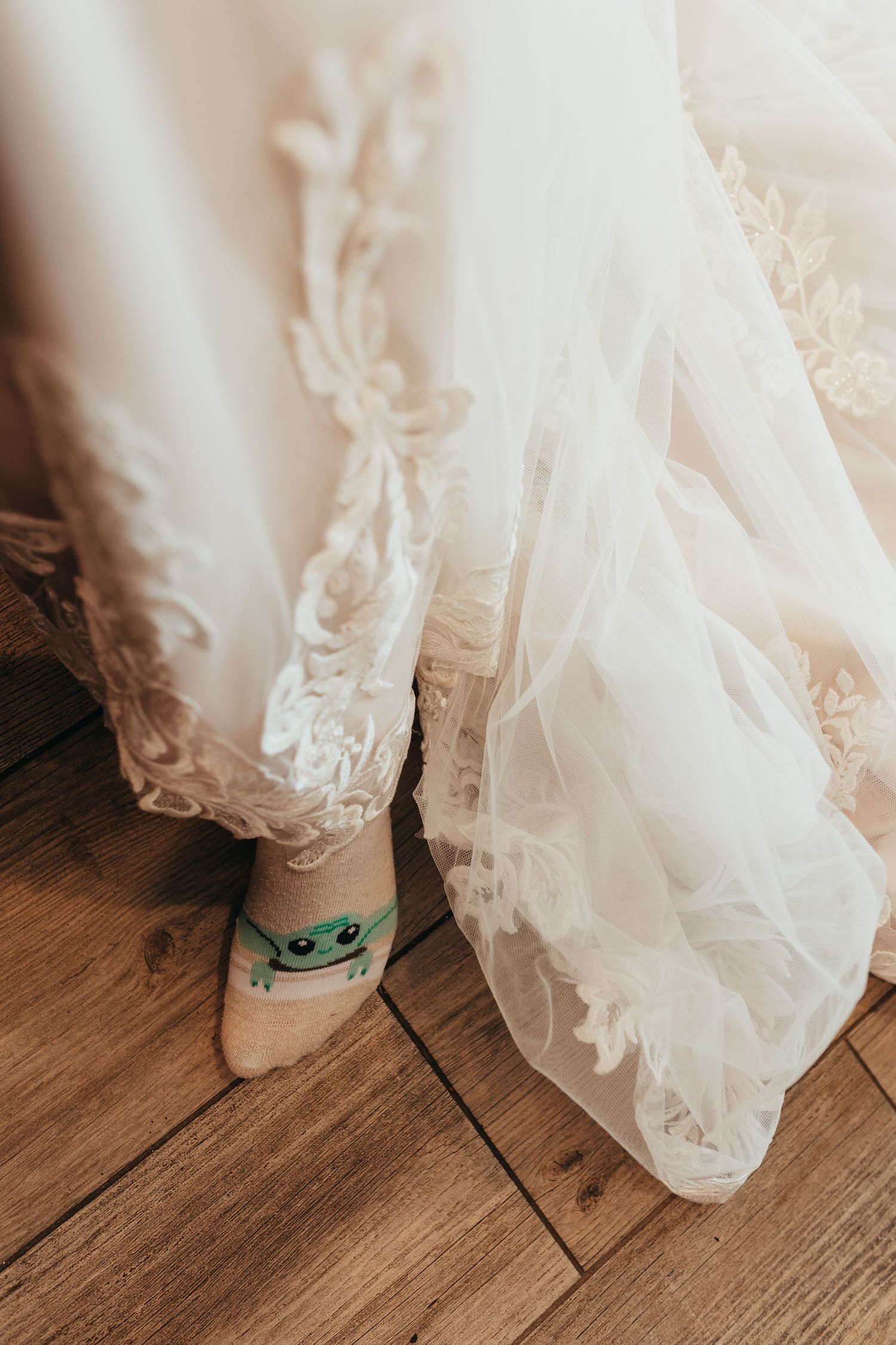 White lace wedding dress hem with decorative socks visible on wooden floor.