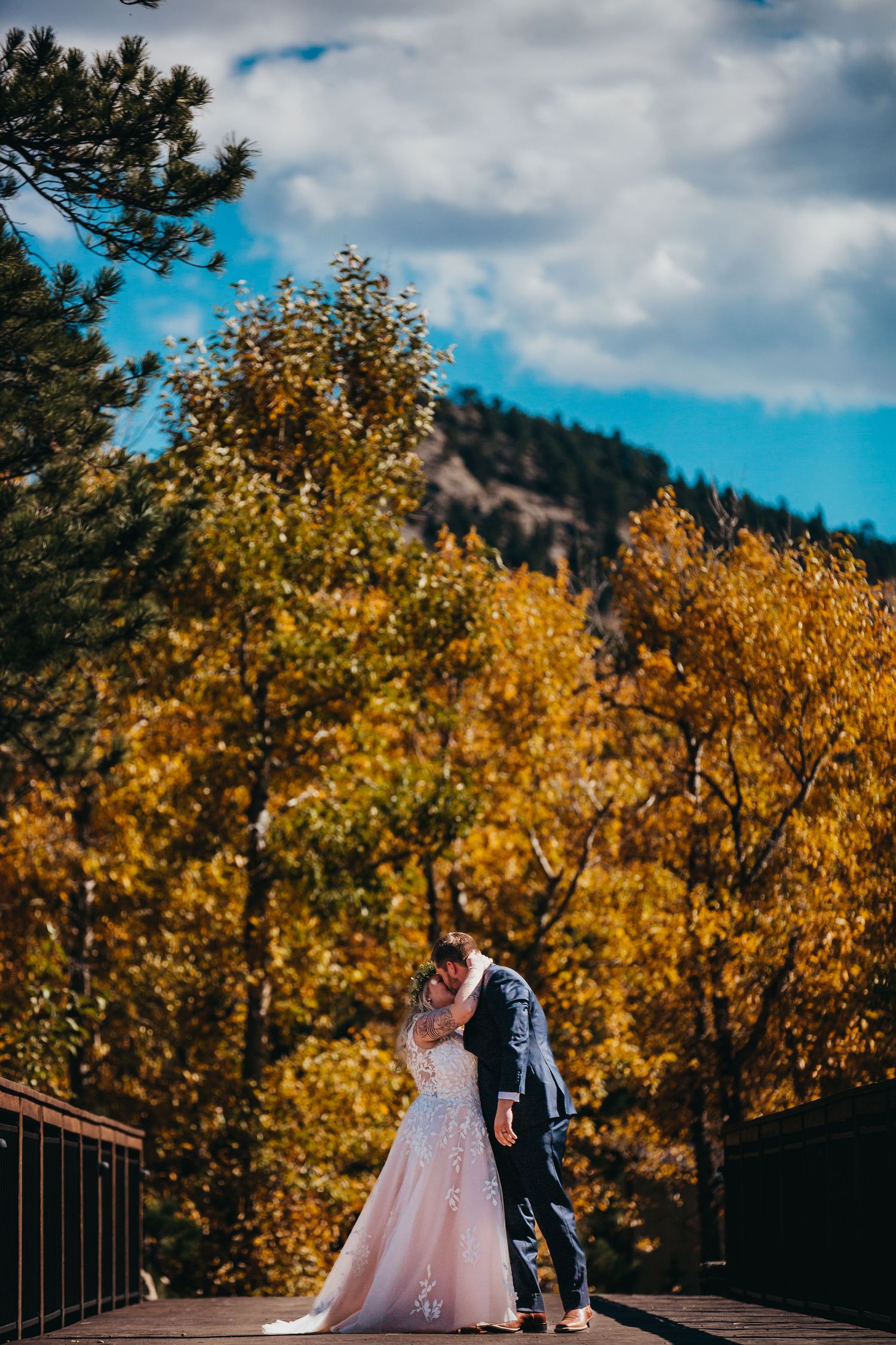 Wedding couple standing on deck surrounded by vibrant fall foliage and mountain scenery.