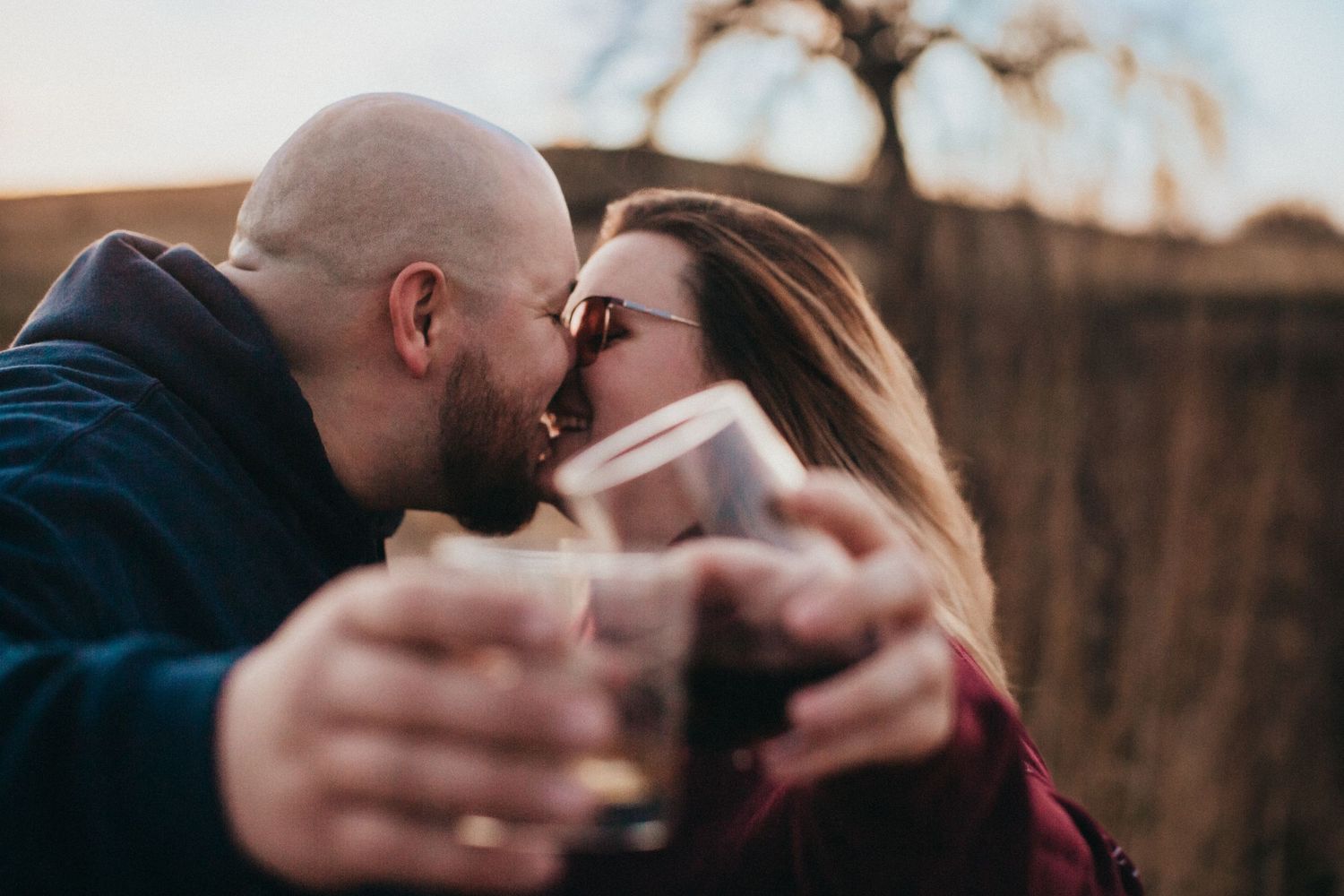 An intimate moment shared between a couple holding coffee cups outdoors.