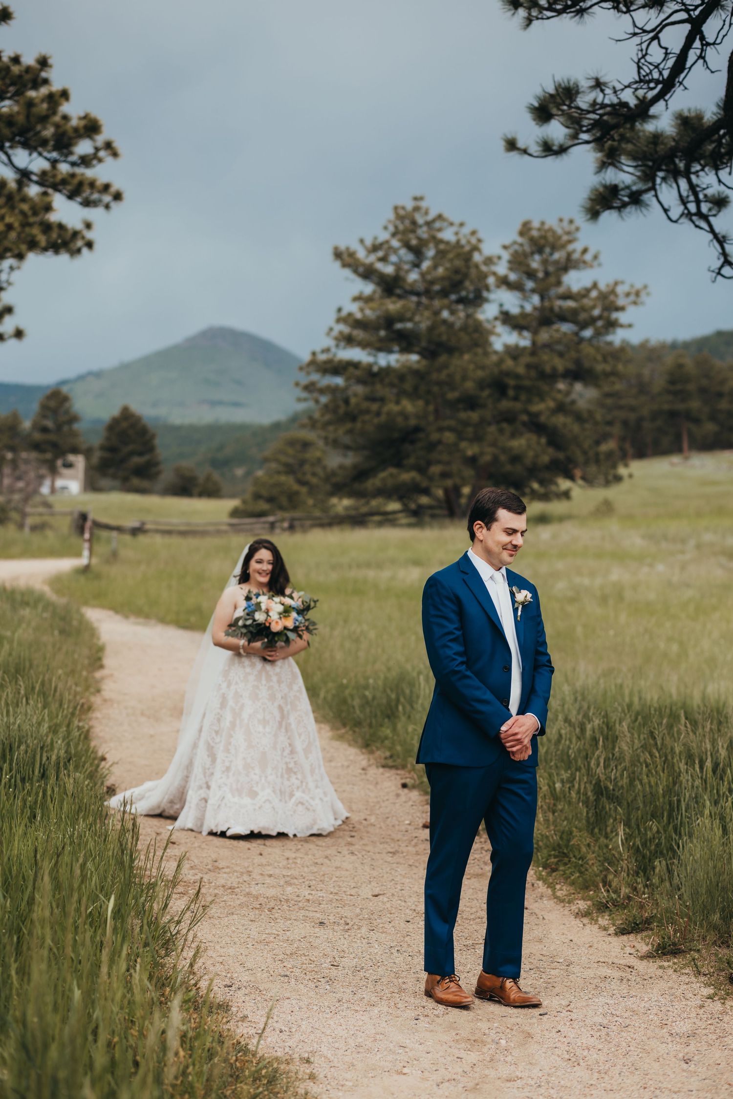 Wedding couple on a mountain trail with pine trees and rolling hills in the background.