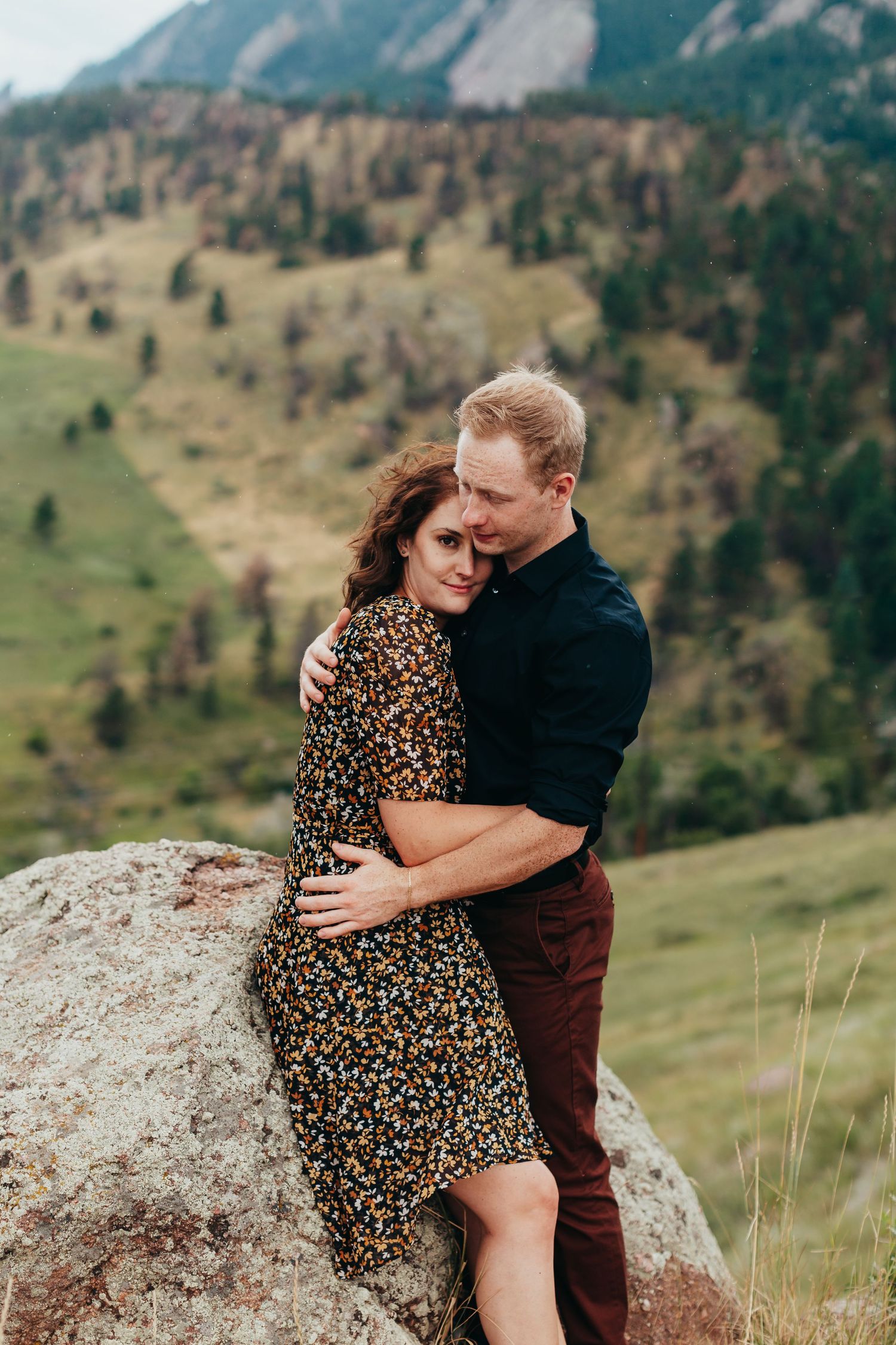 A couple sharing an intimate moment on a rock overlooking mountain landscapes.