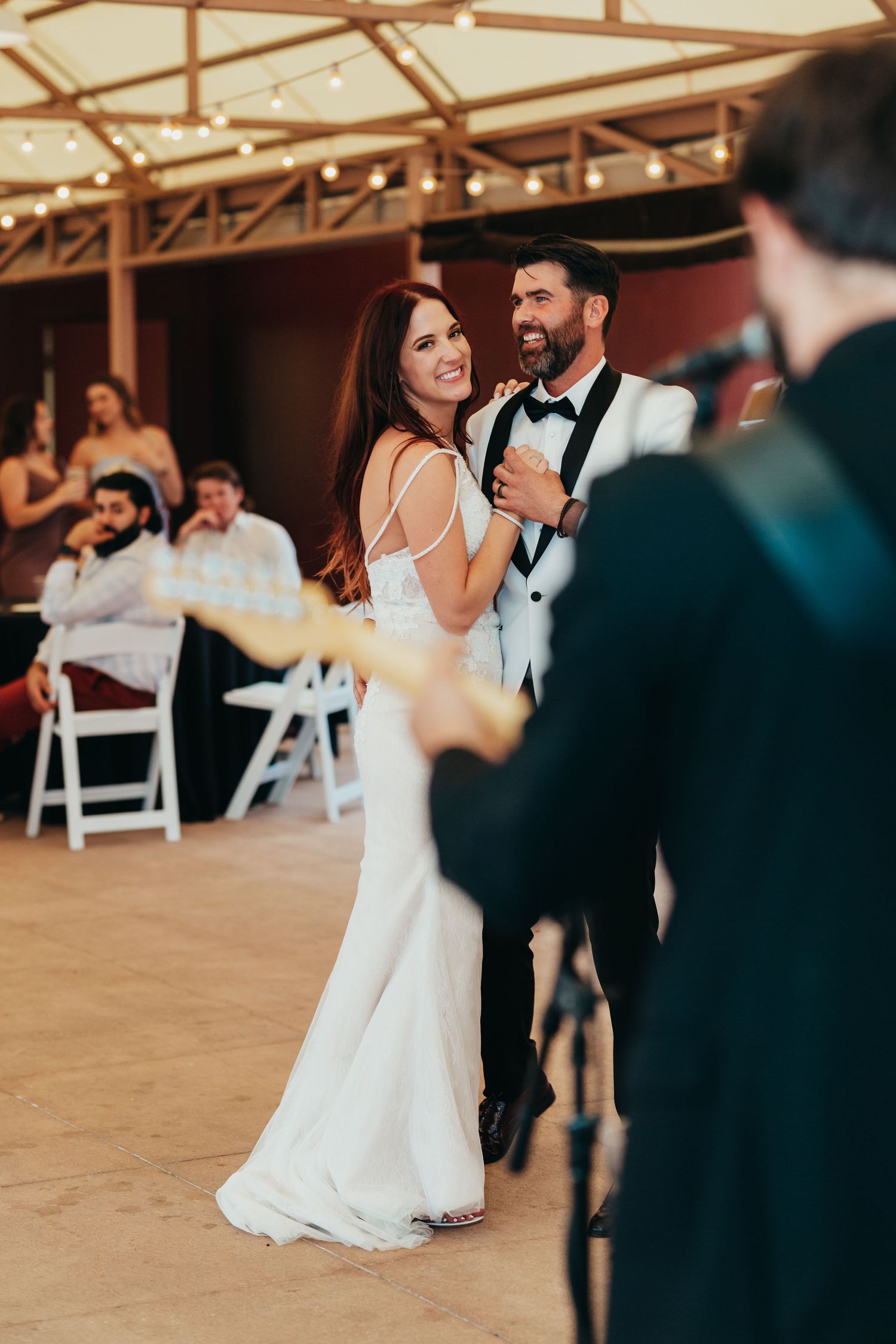 Couple dances together at wedding reception under rustic wooden beams.